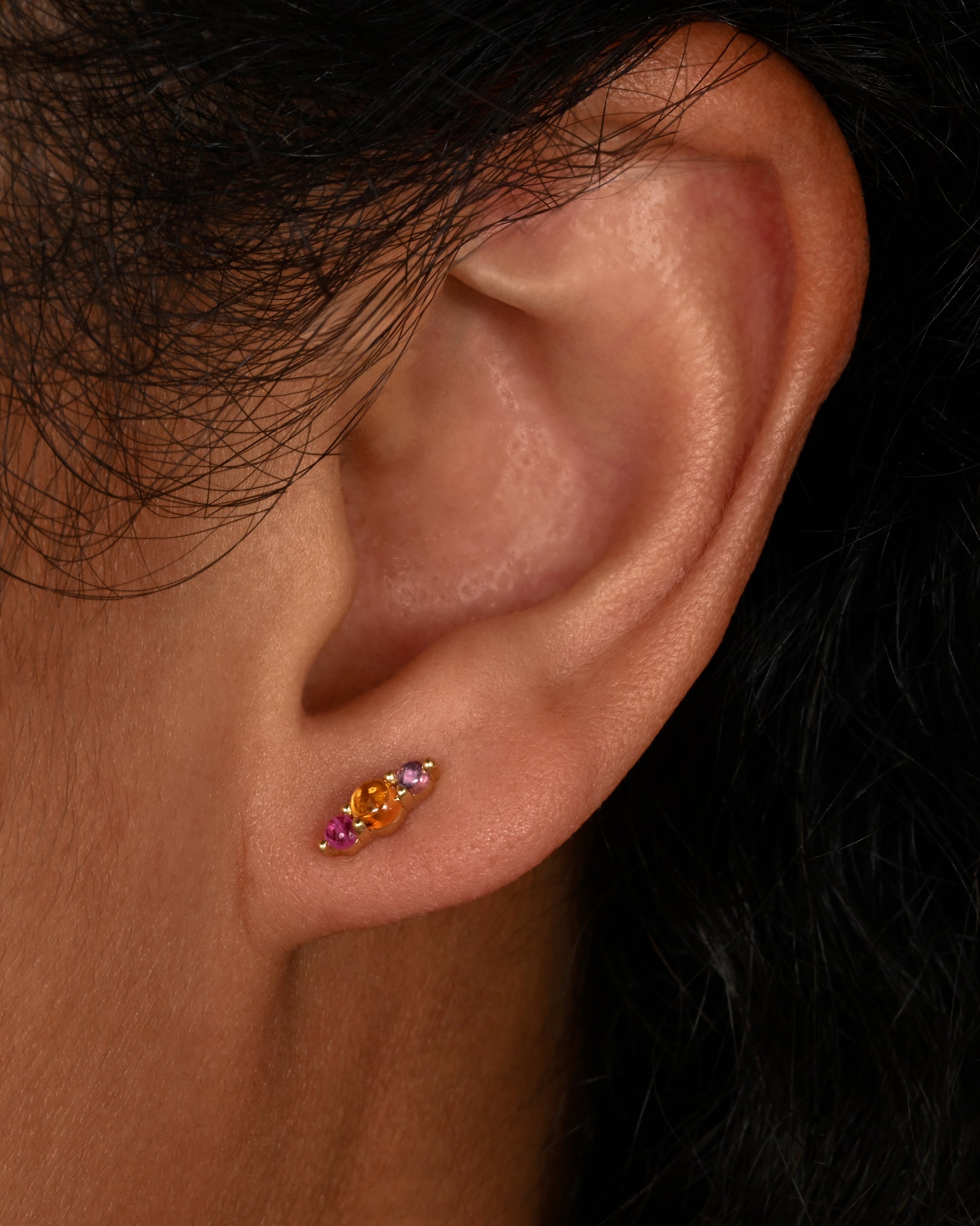 Yellow gold earrings with three sapphires cabochons, shown on an ear.