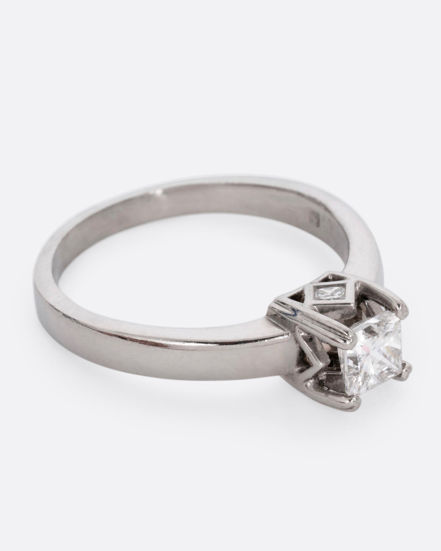 A platinum ring with a princess cut diamond, prong set high above angular cutouts and diamond accents. Shown from the side.