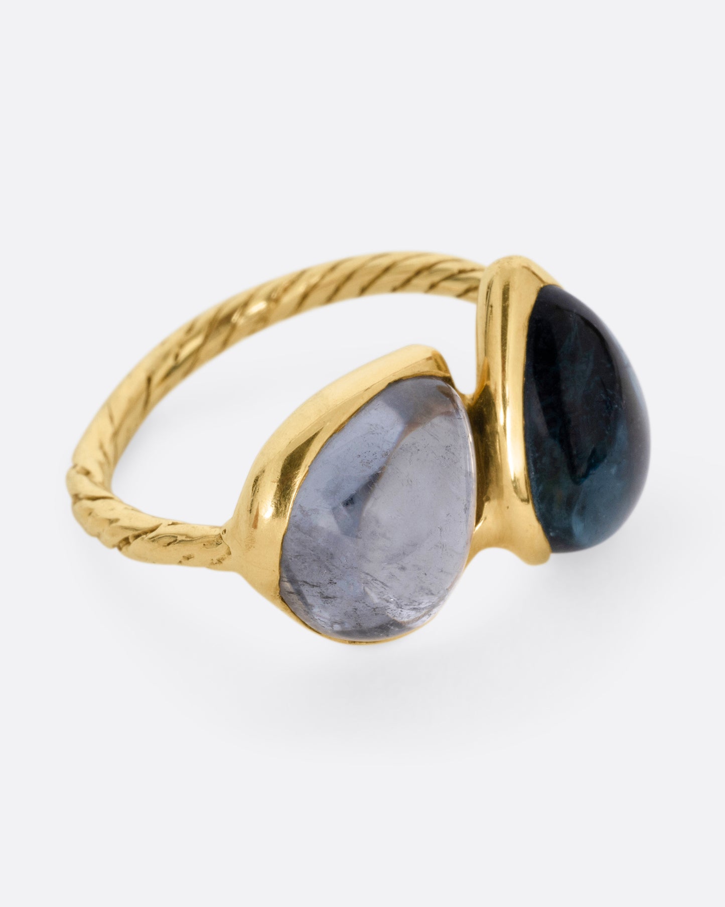A yellow gold ring with a pair of blue green tourmalines and a textured hand- carved band, shown from the side.