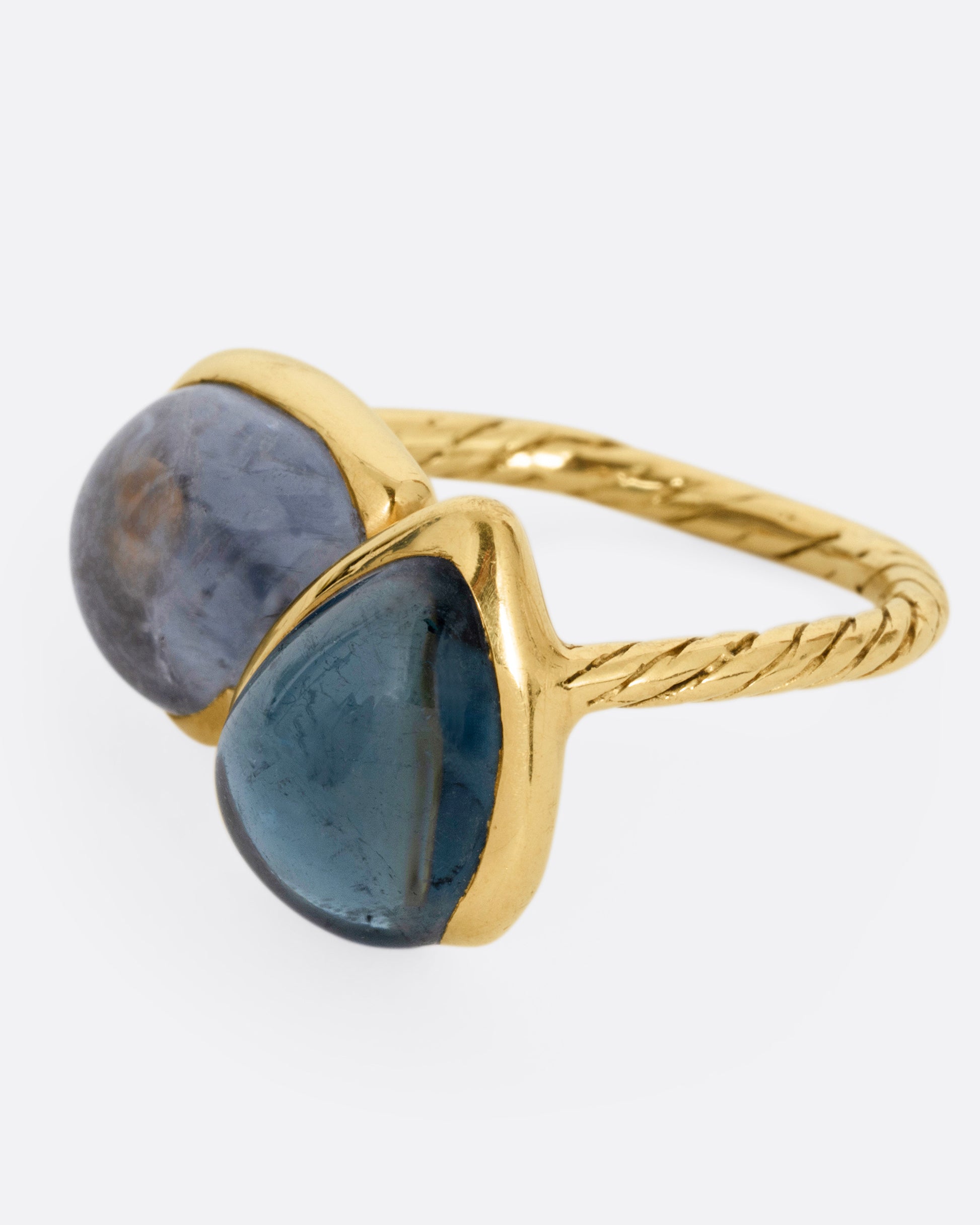 A yellow gold ring with a pair of blue green tourmalines and a textured hand- carved band, shown from the side.