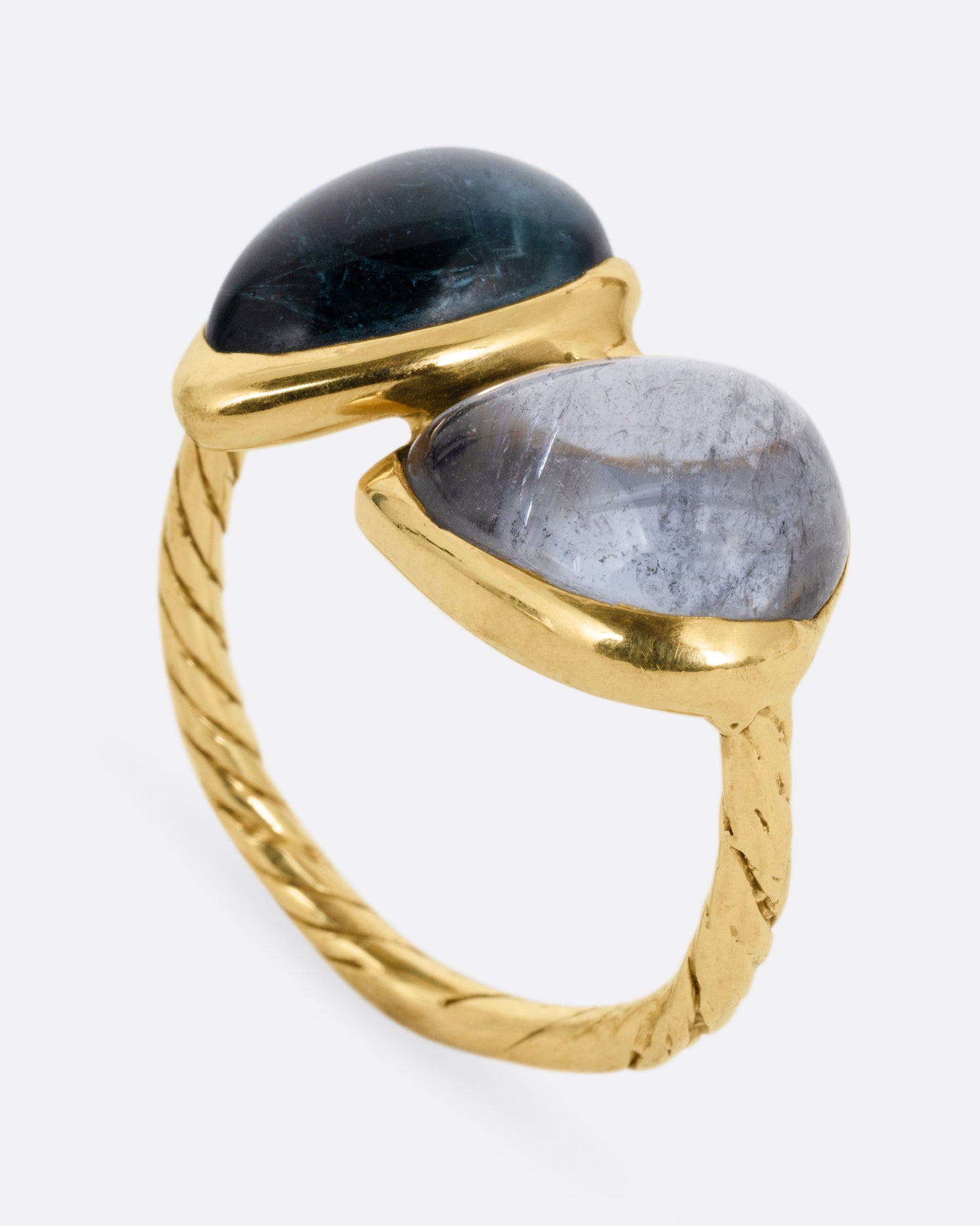 A yellow gold ring with a pair of blue green tourmalines and a textured hand- carved band, shown from the side standing up.