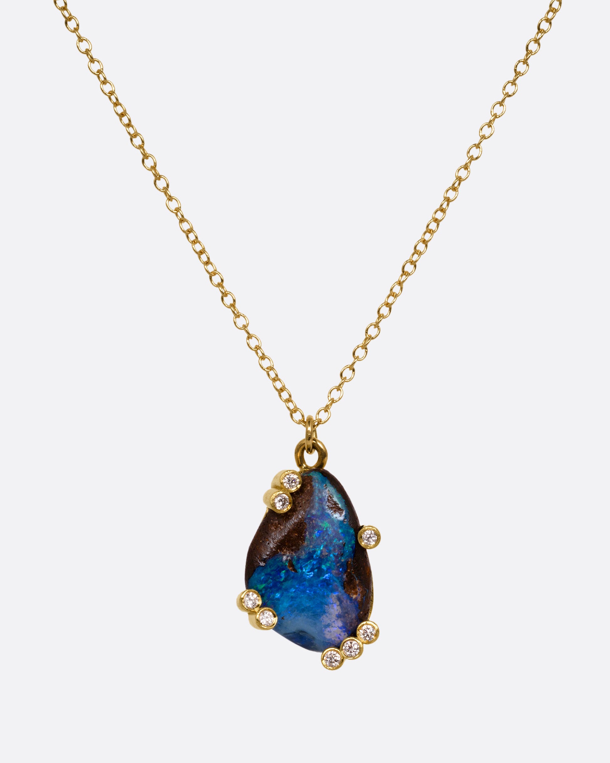 A yellow gold cable chain necklace with diamond studded gold anemones around a free-form boulder opal pendant, shown from the front.