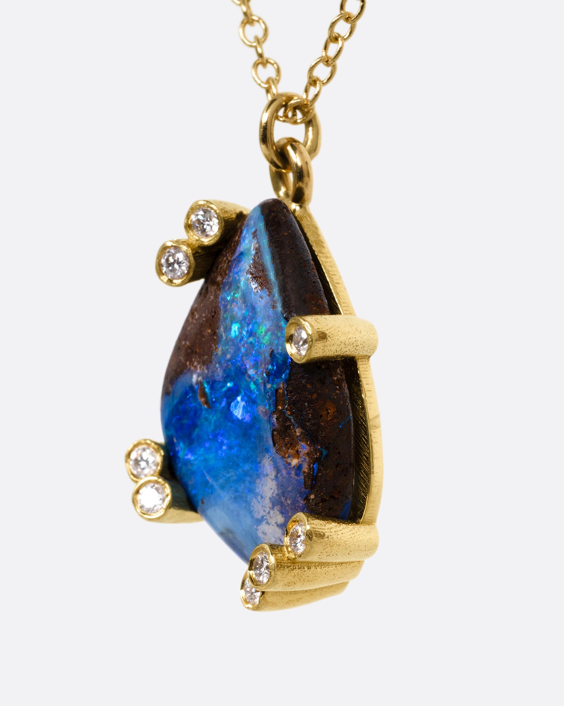 A yellow gold cable chain necklace with diamond studded gold anemones around a free-form boulder opal pendant, shown from the side.