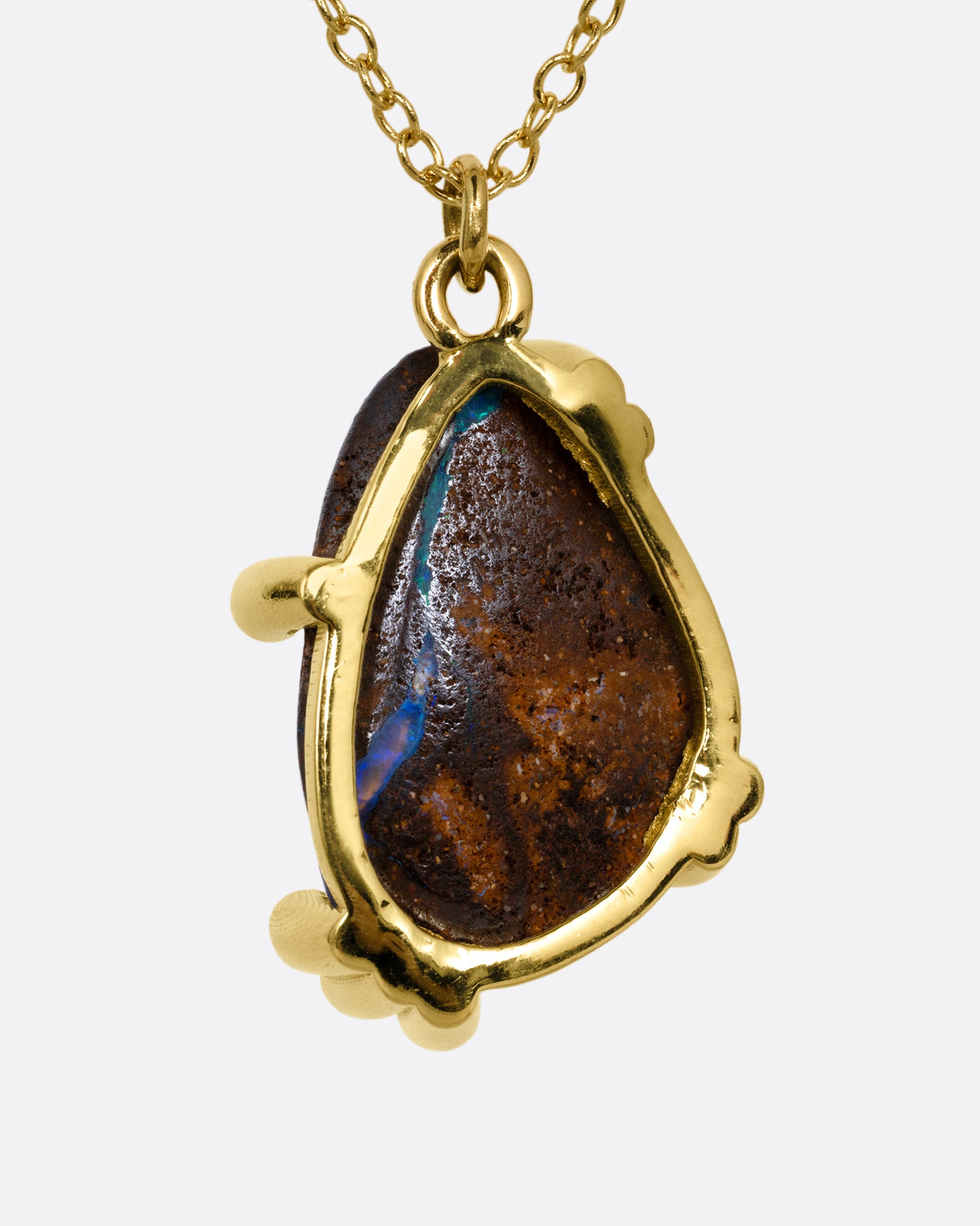 A yellow gold cable chain necklace with diamond studded gold anemones around a free-form boulder opal pendant, shown from the back.