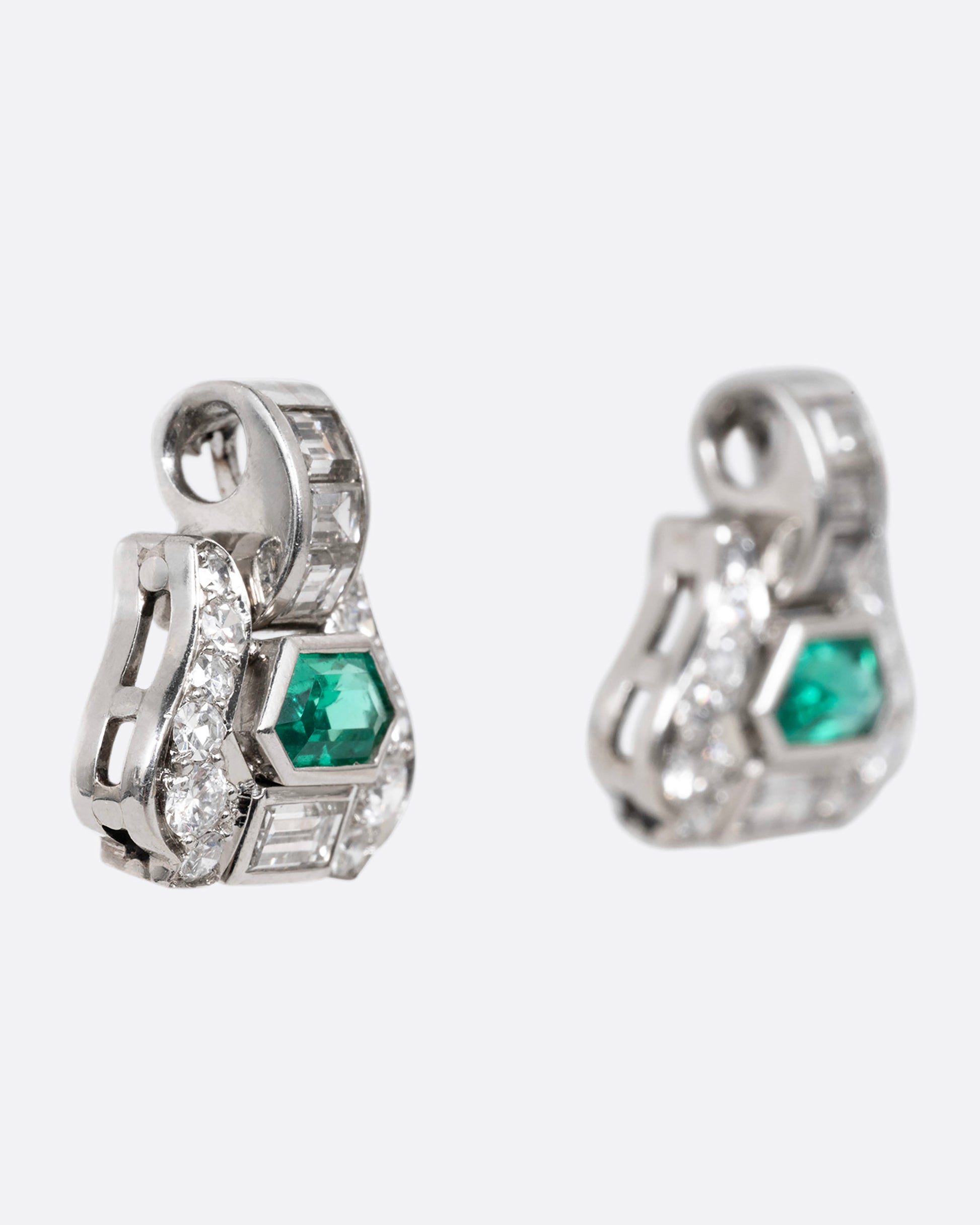A pair of platinum earrings with emeralds and diamonds, shown from the side.