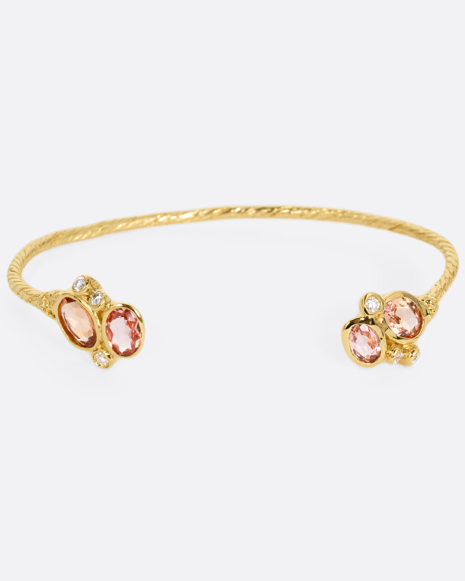 A yellow gold hand carved cuff bracelet with clusters of tourmalines and diamonds on either side of its open front, shown from the front.