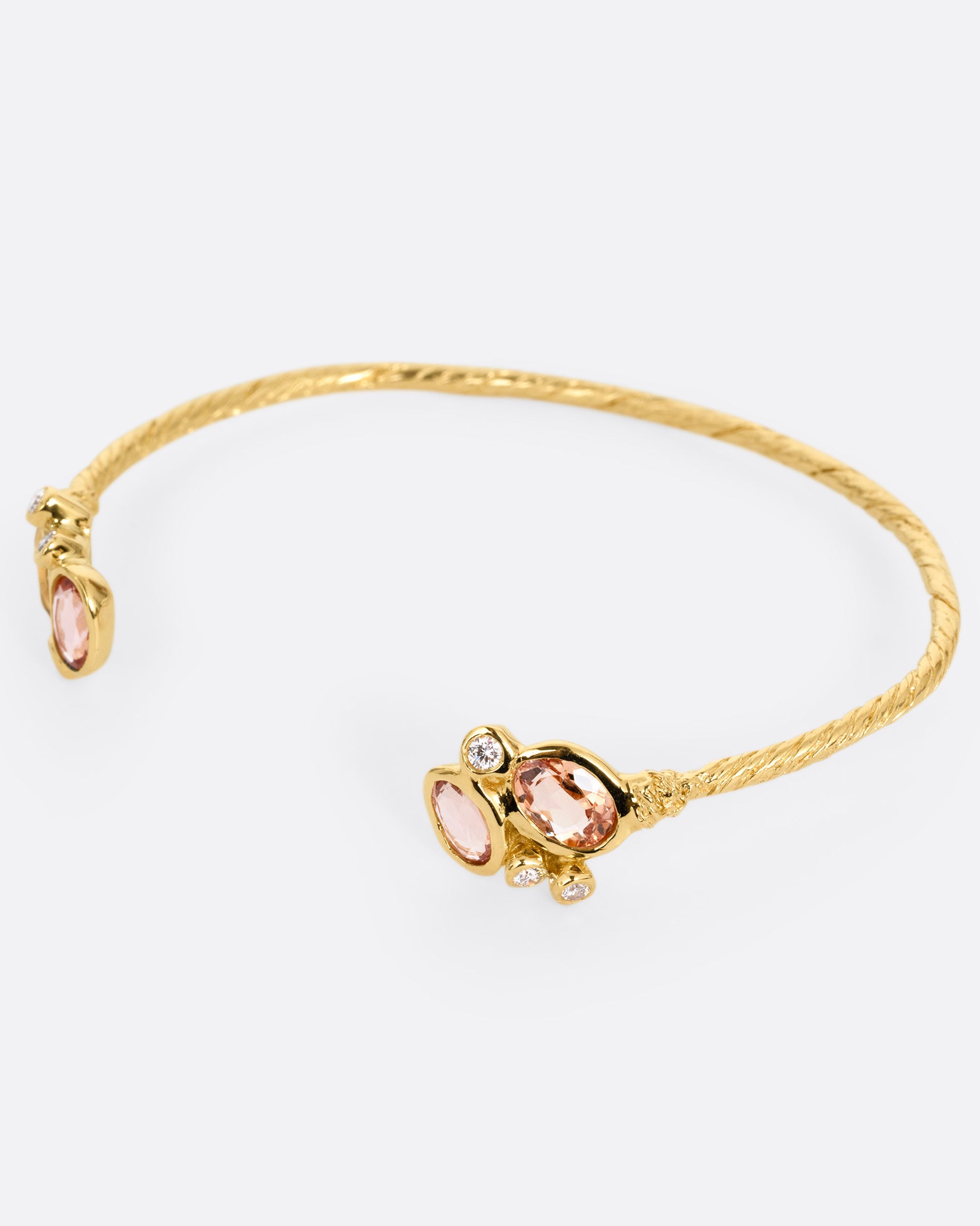 A yellow gold hand carved cuff bracelet with clusters of tourmalines and diamonds on either side of its open front, shown from the side.