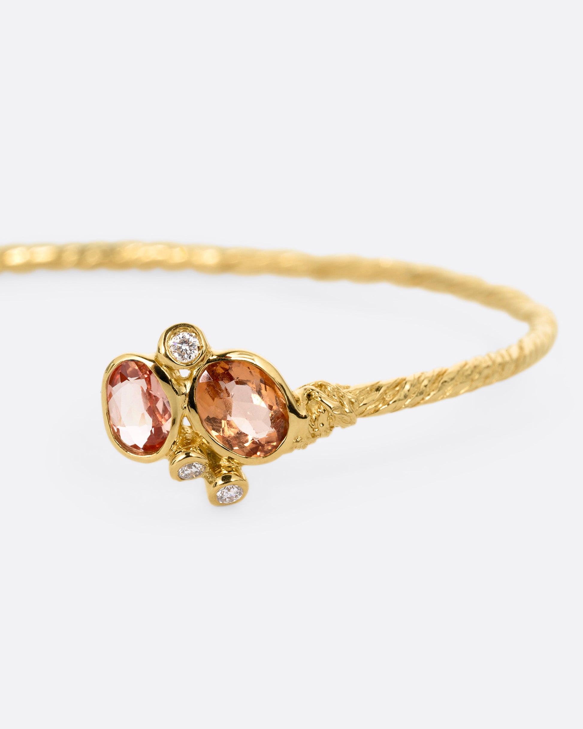A close up of a yellow gold hand carved cuff bracelet with clusters of tourmalines and diamonds on either side of its open front.