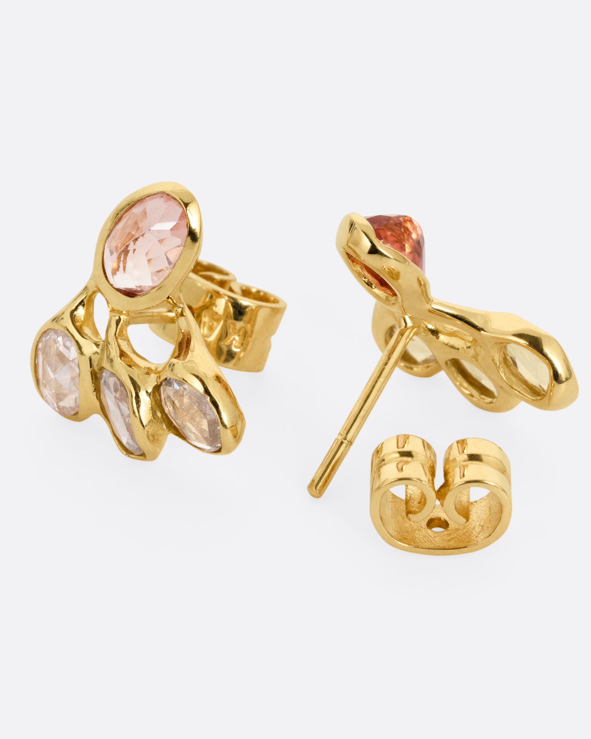 A pair of yellow gold stud earrings with freeform rose cut diamonds and pink tourmalines. One earring is shown from the front, the other open from the back.