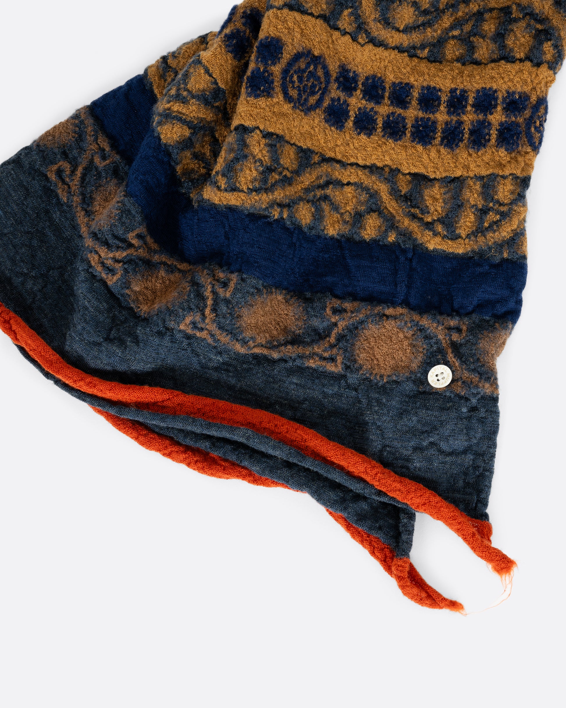 A navy blue and grey scarf with a golden yellow skull in the center. View close up of the hem.