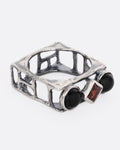 A silver square cage ring with two onyx cabochons bookending a princess cut garnet, shown from the side.