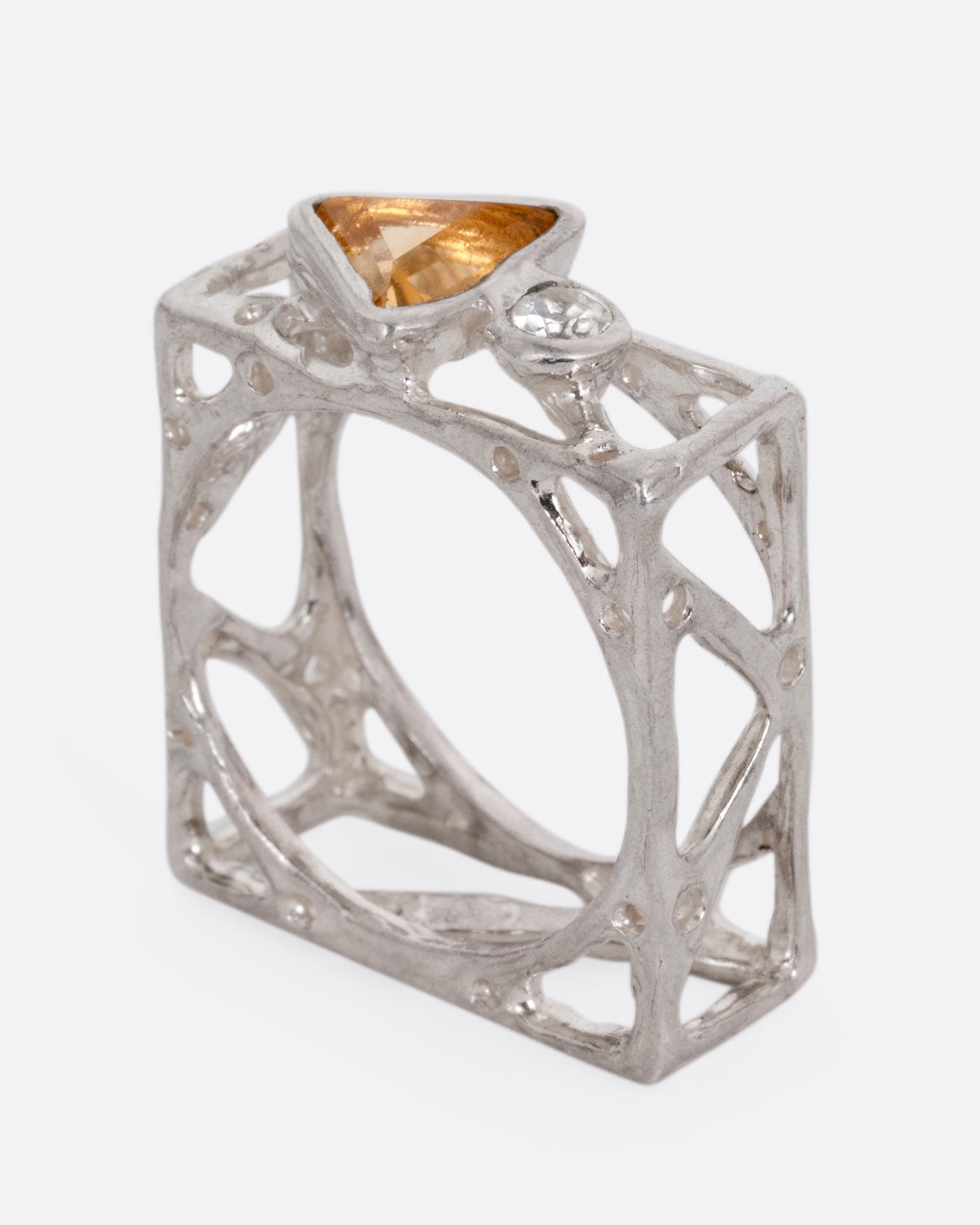 A silver stacked square ring with cutouts and a triangular citrine and a round topaz, shown from the side standing up.
