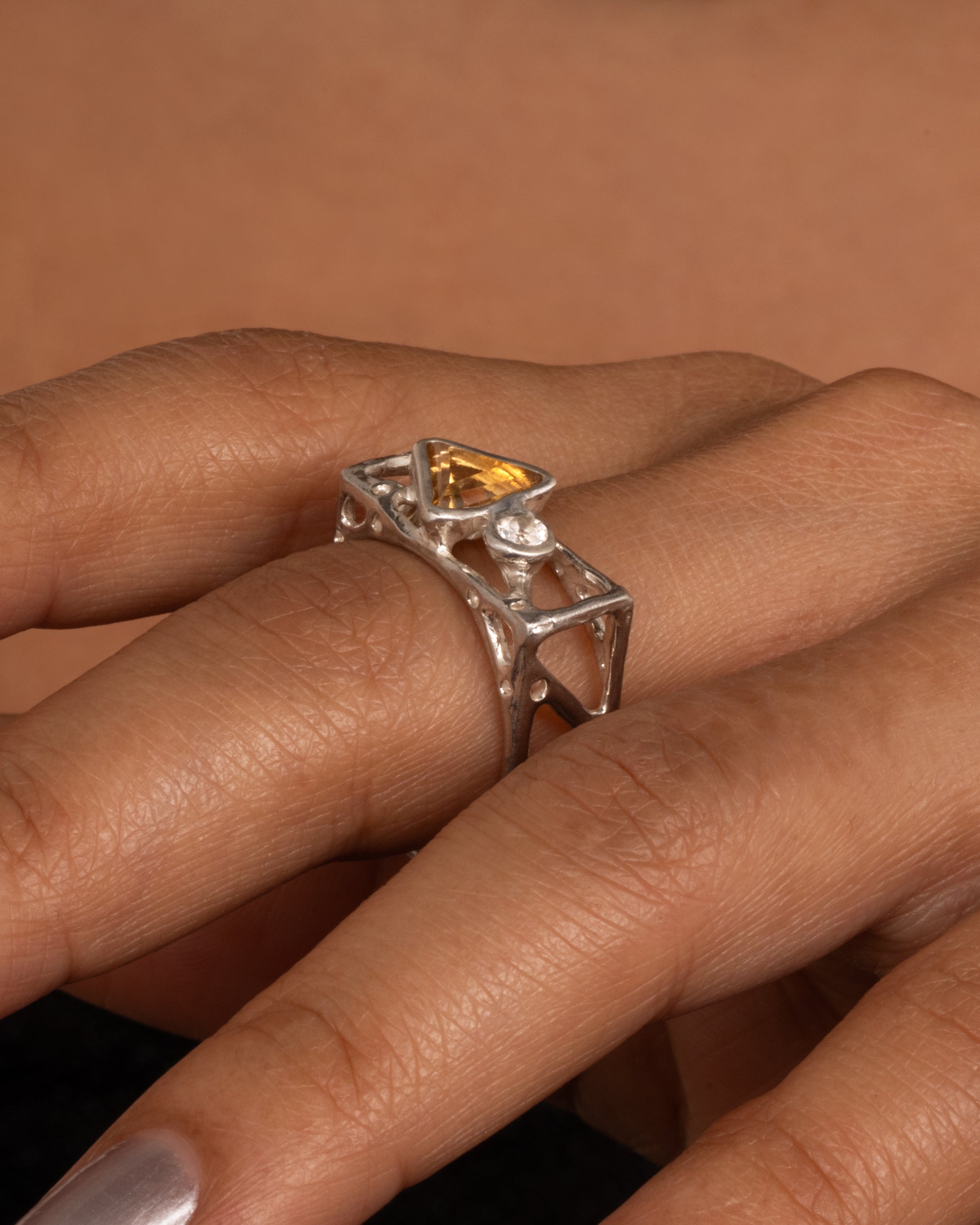 A silver stacked square ring with cutouts and a triangular citrine and a round topaz, shown on a hand.