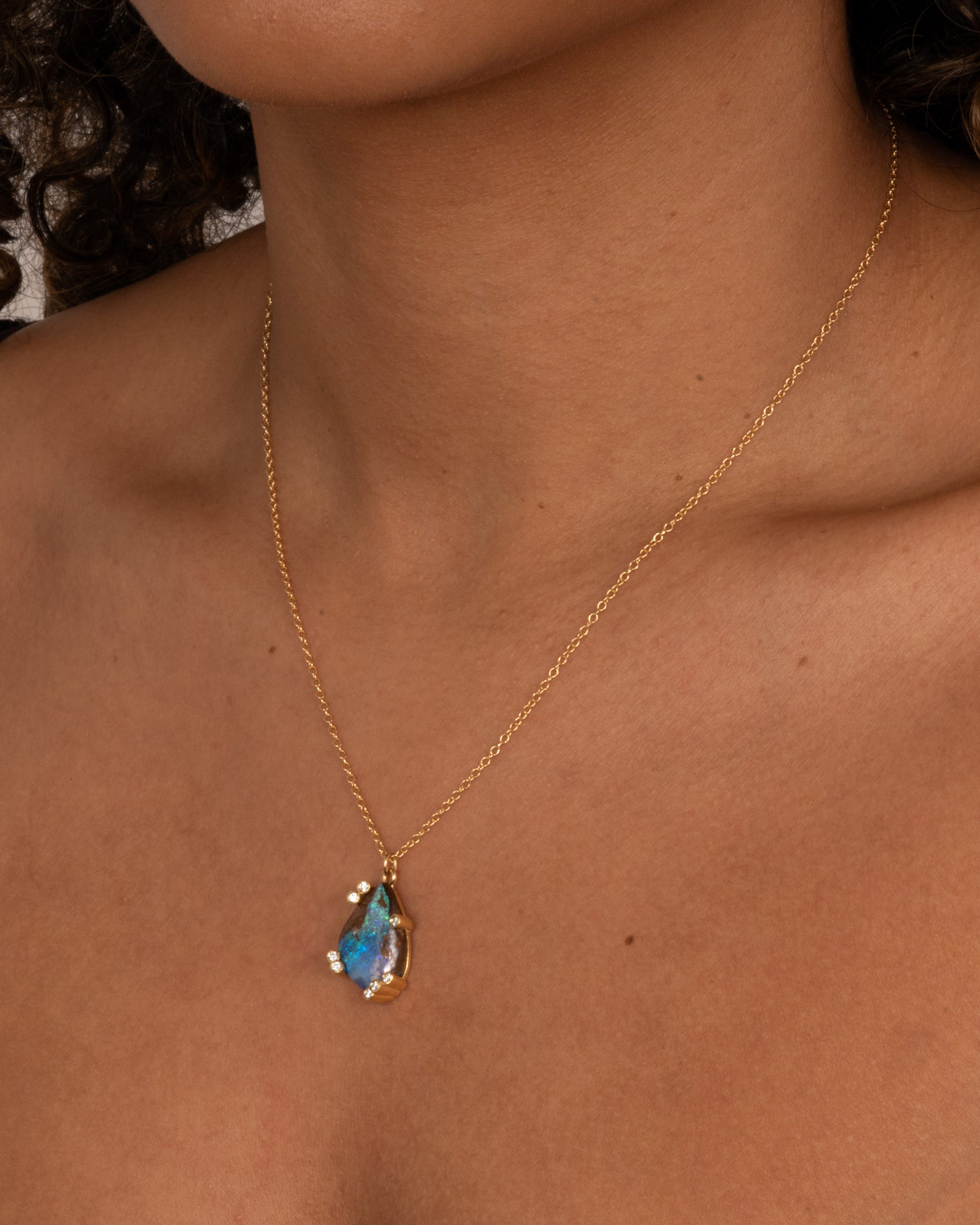 A yellow gold cable chain necklace with diamond studded gold anemones around a free-form boulder opal pendant, shown on a person.