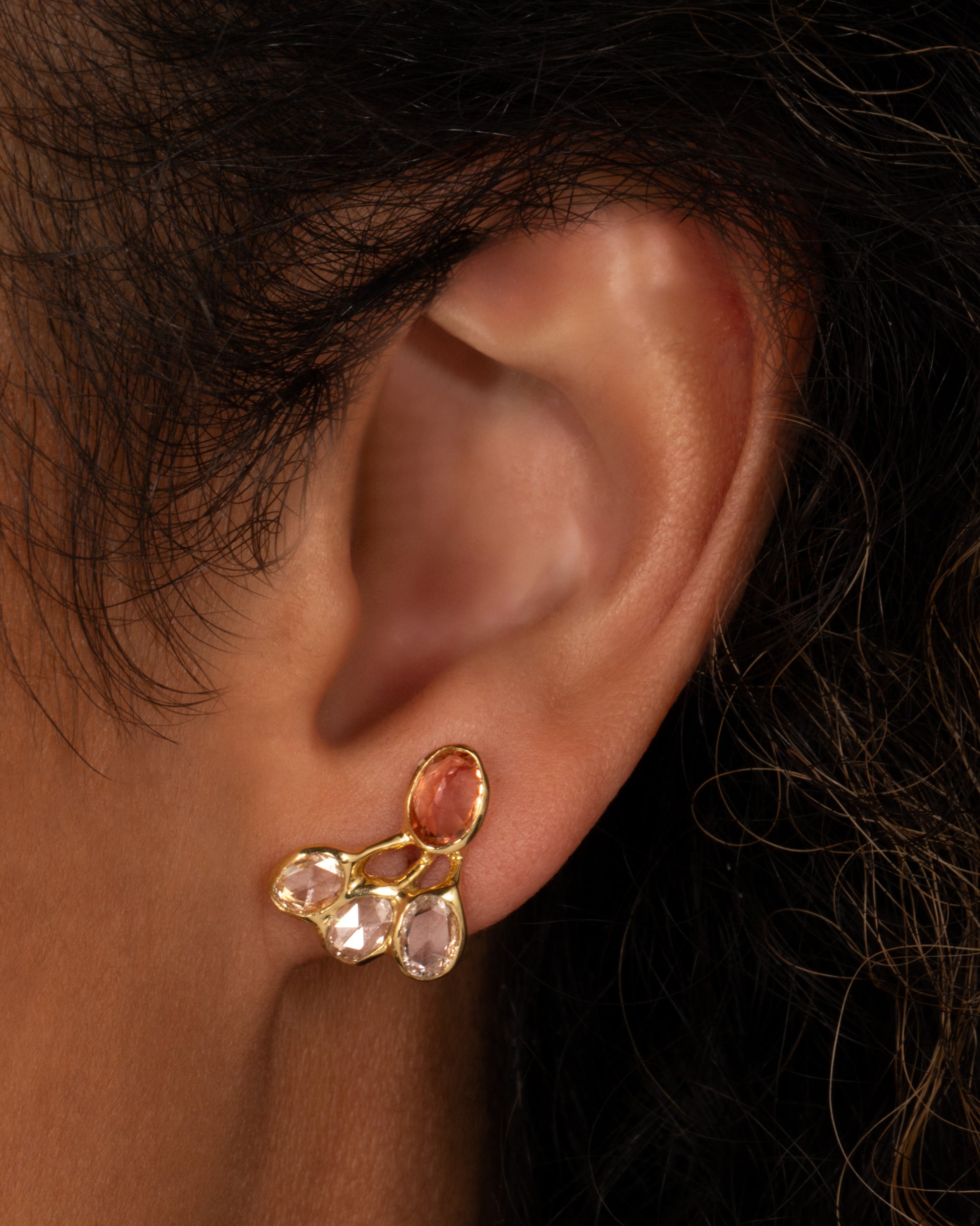 A yellow gold stud earring with freeform rose cut diamonds and pink tourmalines, shown on a person.