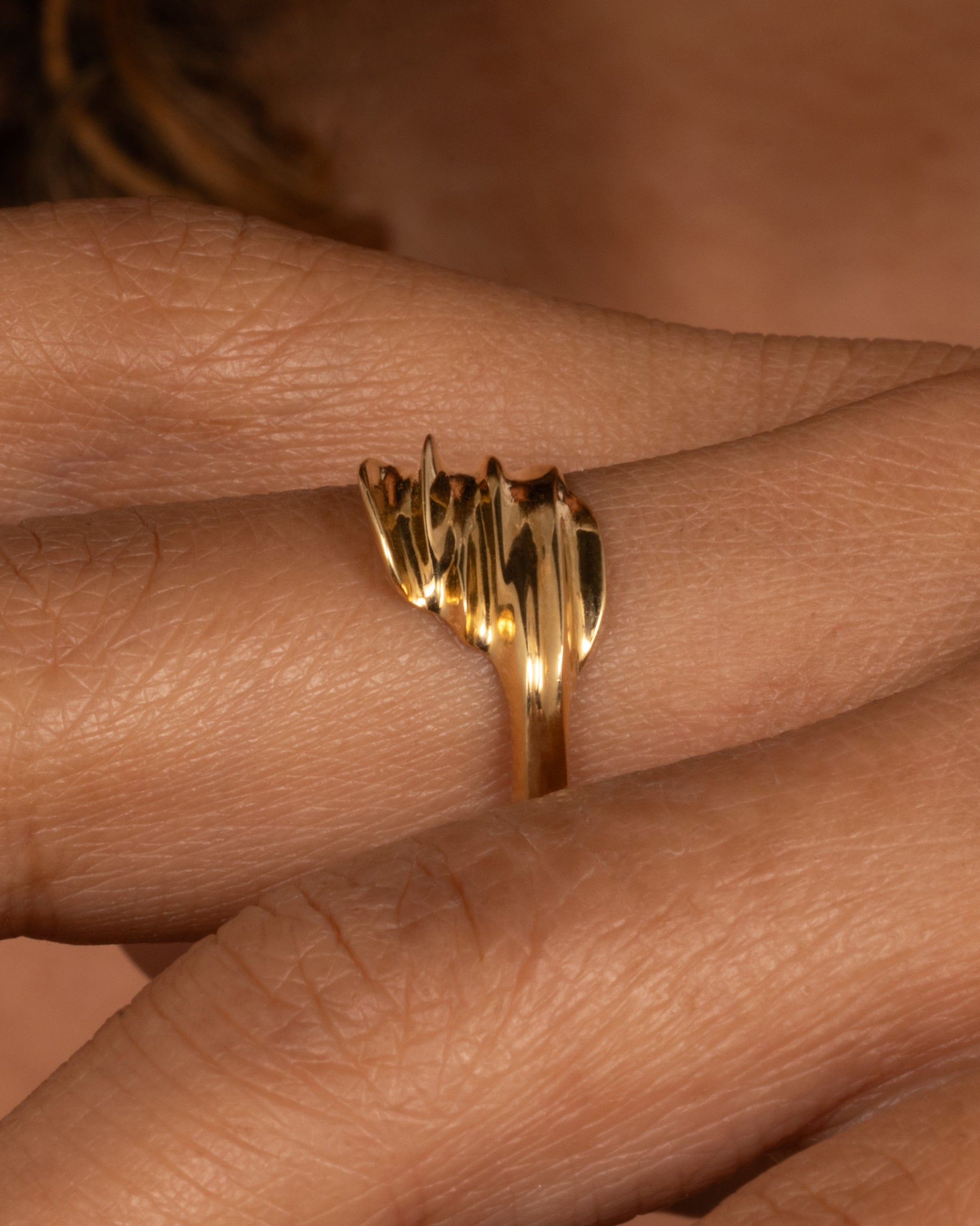 A yellow gold ring with a fluid, dimensional silhouette and narrow back, shown from the side on a hand.