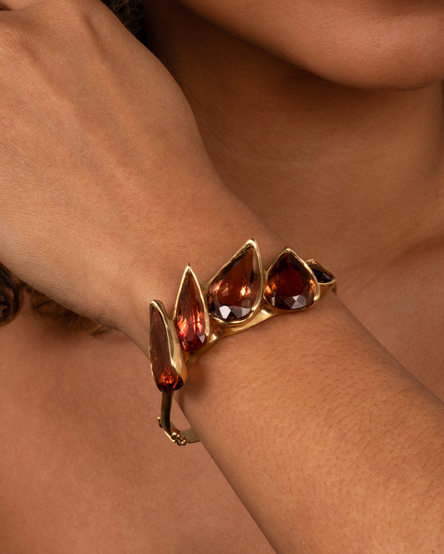 A yellow gold bracelet with five teardrop shaped tourmalines, shown on a person.