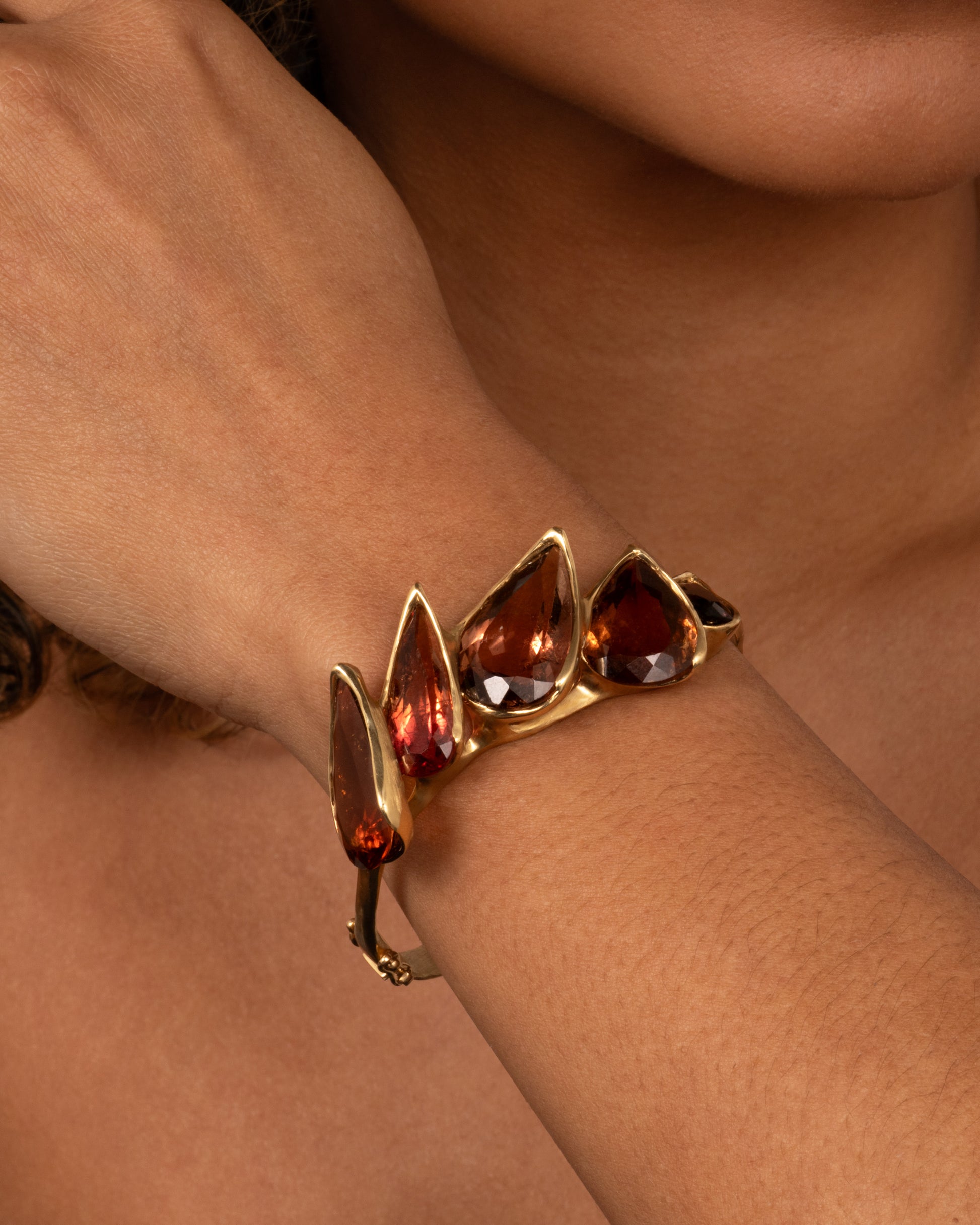 A yellow gold bracelet with five teardrop shaped tourmalines, shown on a person.