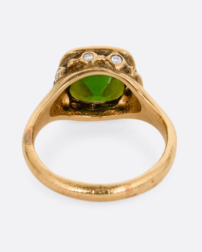 A yellow gold ring with a deep green tourmaline and white diamonds accents around its rounded edges. Shown from the back.