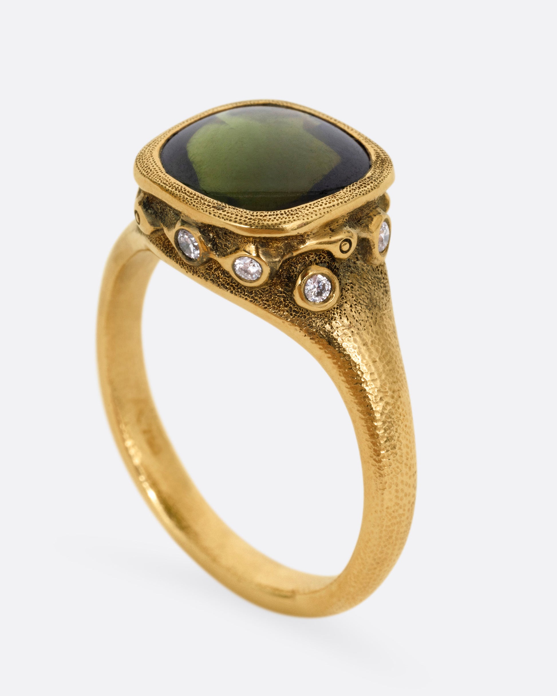 A yellow gold ring with a deep green tourmaline and white diamonds accents around its rounded edges. Shown from the side standing up.