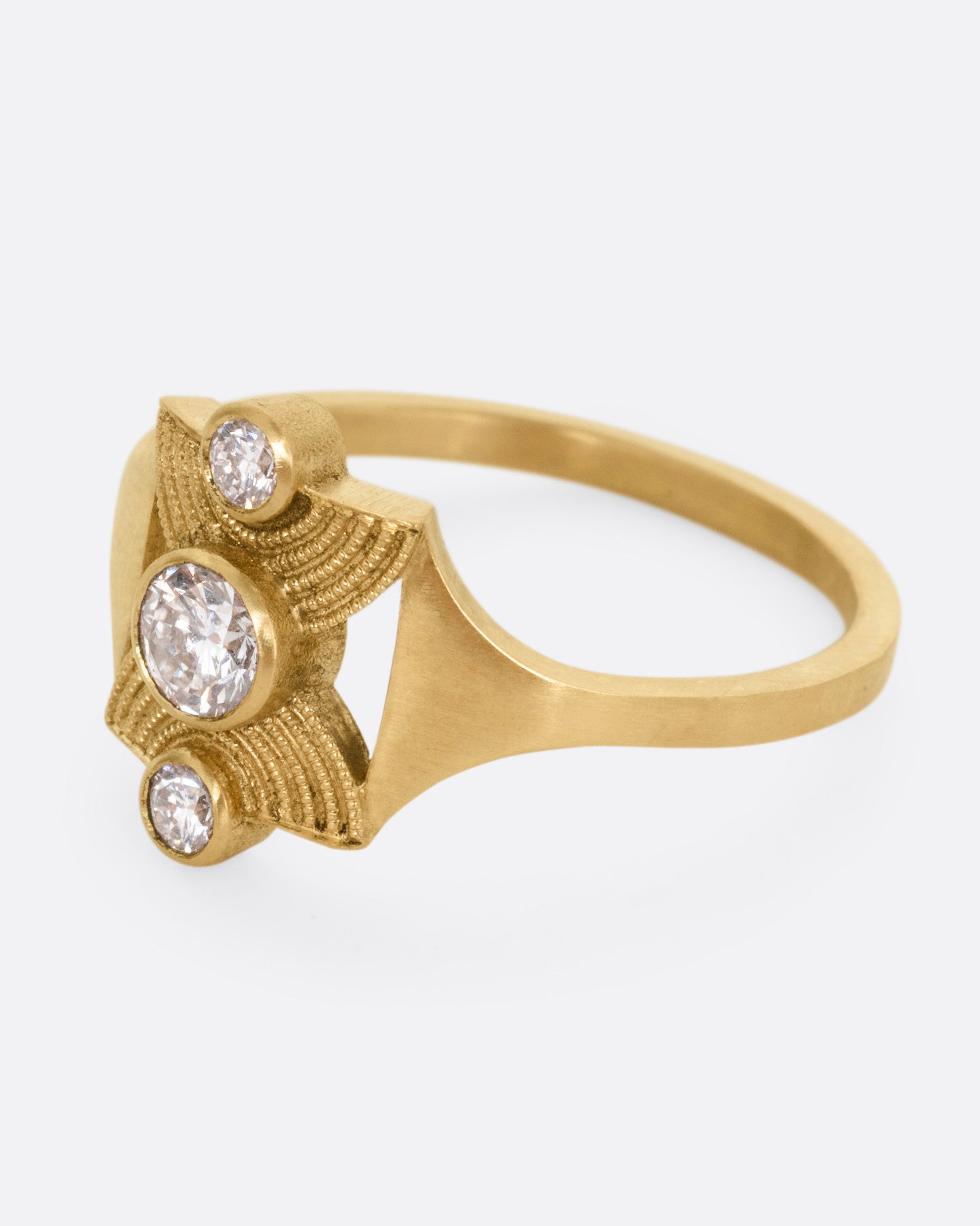 A yellow gold ring with an hourglass shape and three bezel set diamonds, shown from the side.