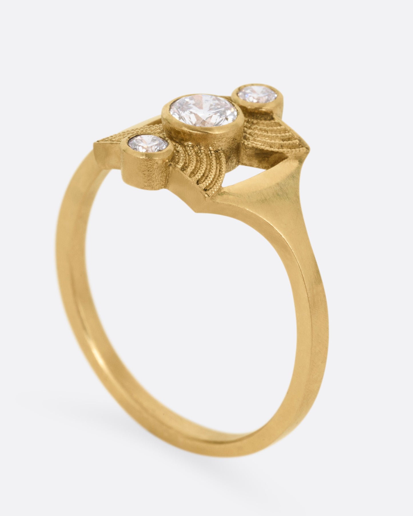 A yellow gold ring with an hourglass shape and three bezel set diamonds, shown from the side standing up.