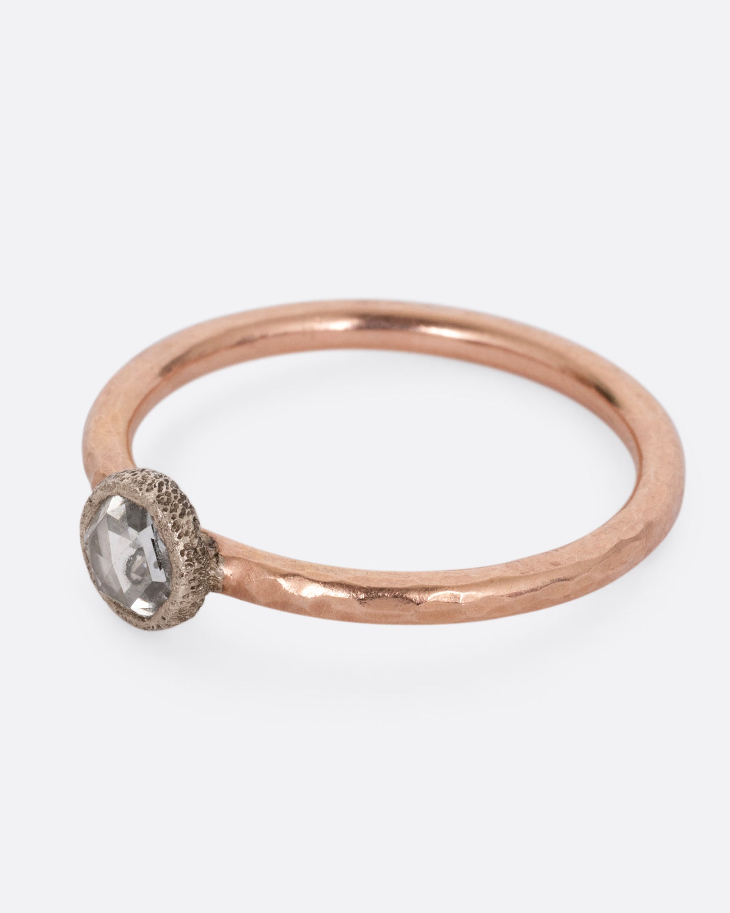 A rose gold ring with a diamond, shown from the side.