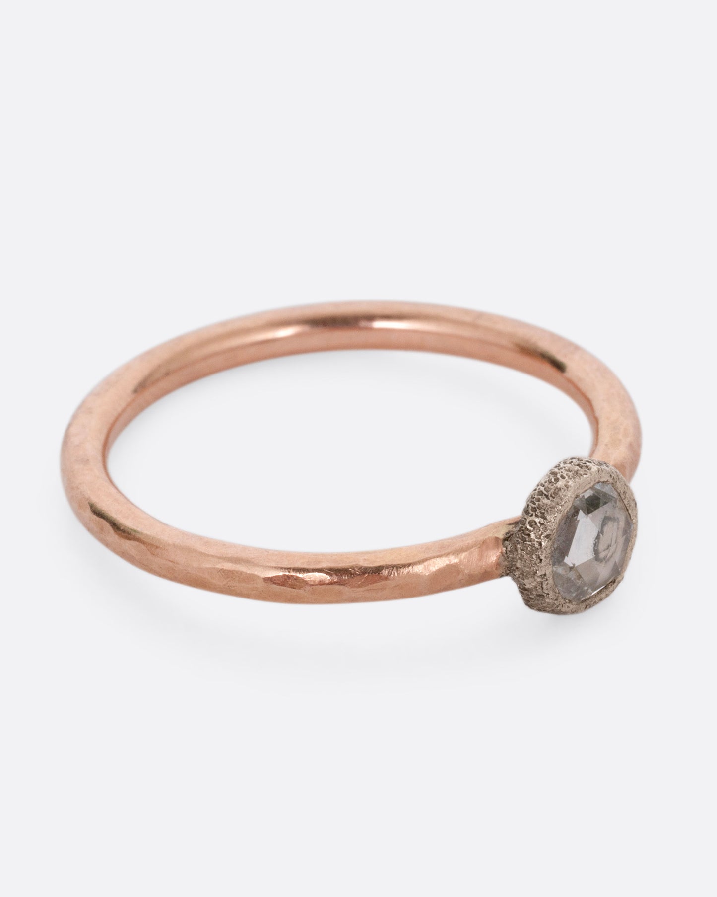 A rose gold ring with a diamond, shown from the side.