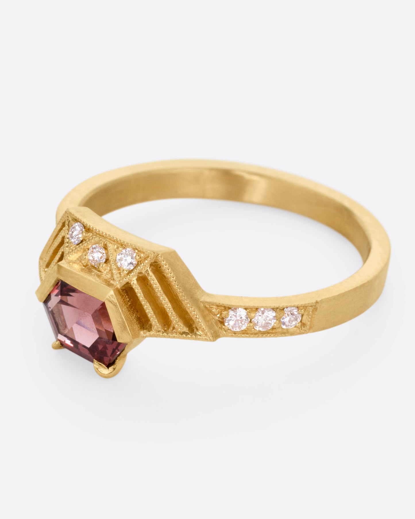 A yellow gold ring with diamond accents, linear cutouts, and a red spinel, shown from the side.