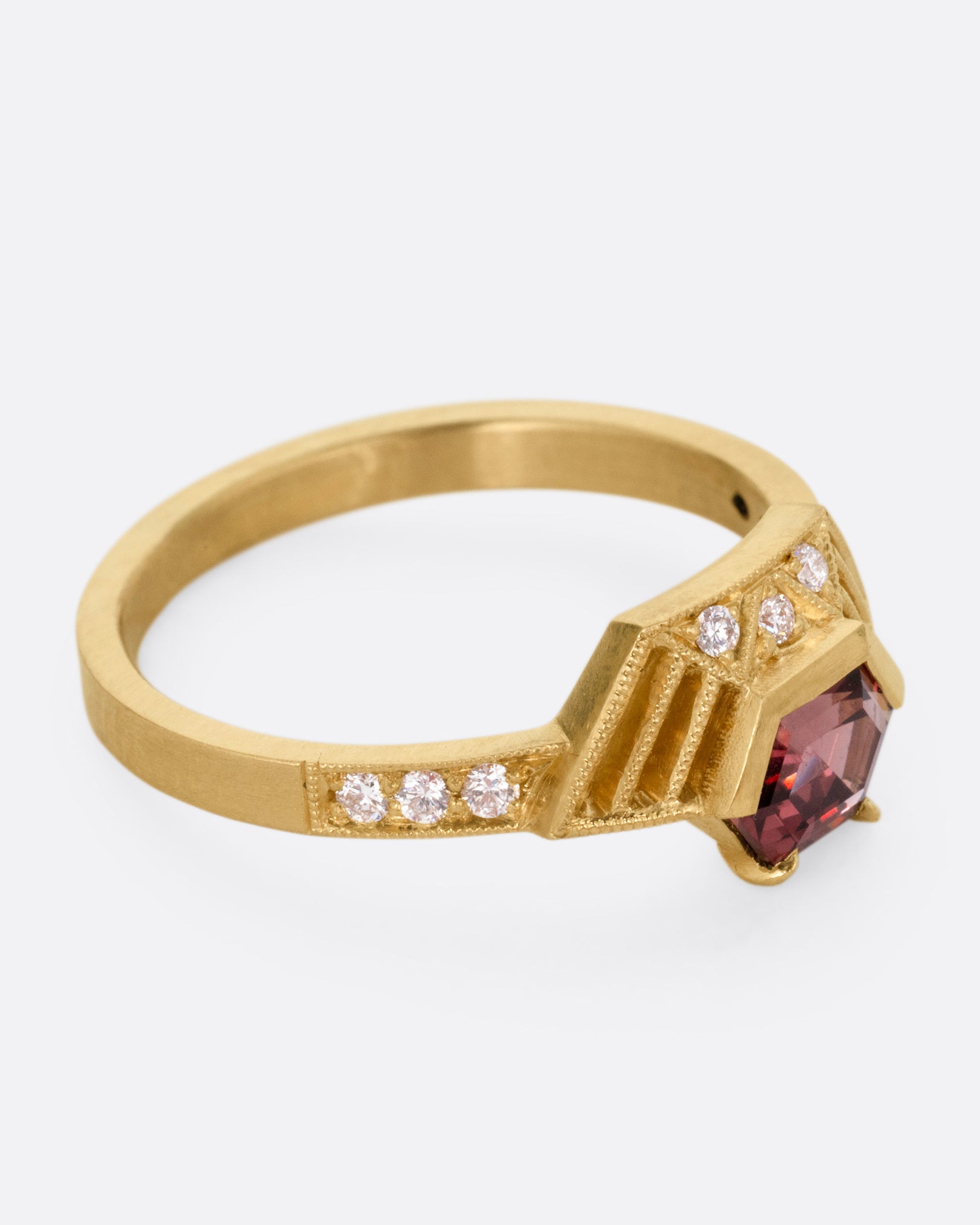 A yellow gold ring with diamond accents, linear cutouts, and a red spinel, shown from the side.