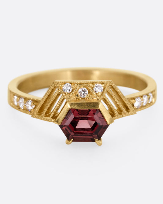 A yellow gold ring with diamond accents, linear cutouts, and a red spinel, shown from the front.