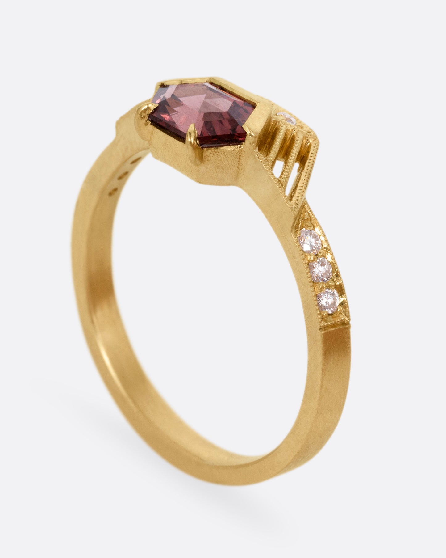 A yellow gold ring with diamond accents, linear cutouts, and a red spinel, shown from the side standing up.