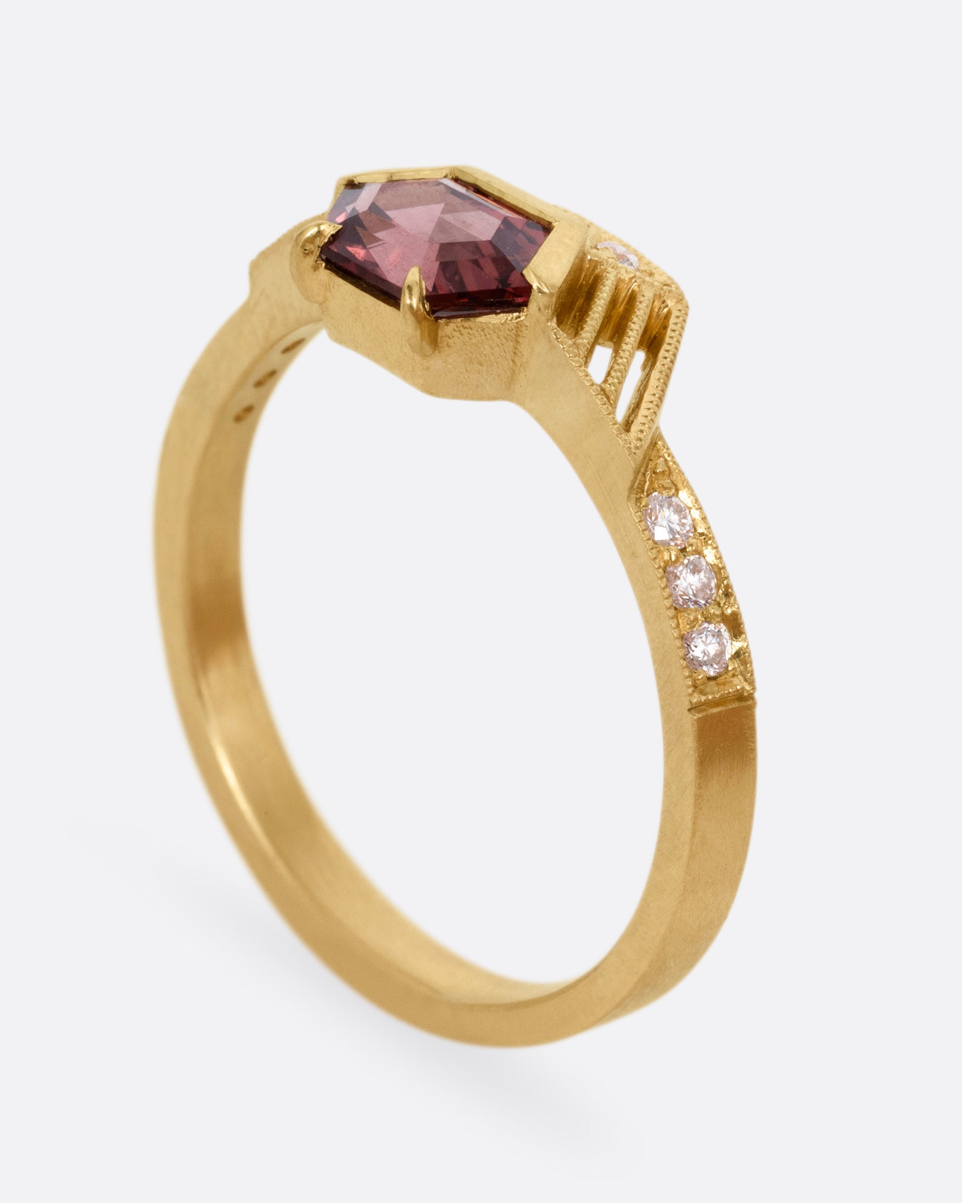 A yellow gold ring with diamond accents, linear cutouts, and a red spinel, shown from the side standing up.