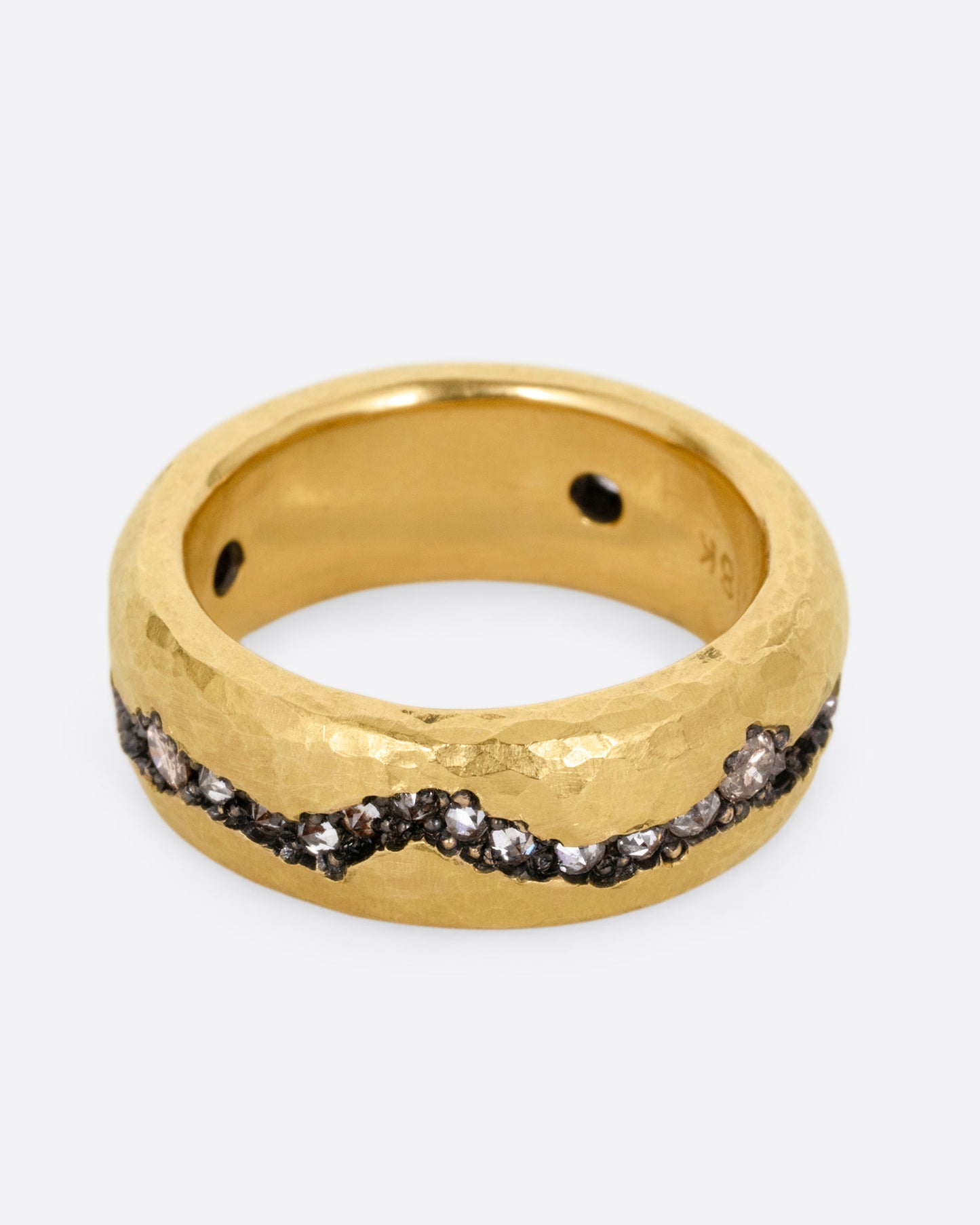 A yellow gold hammered ring with a fissure lined with brown and white diamonds, some reverse set, shown from the front.