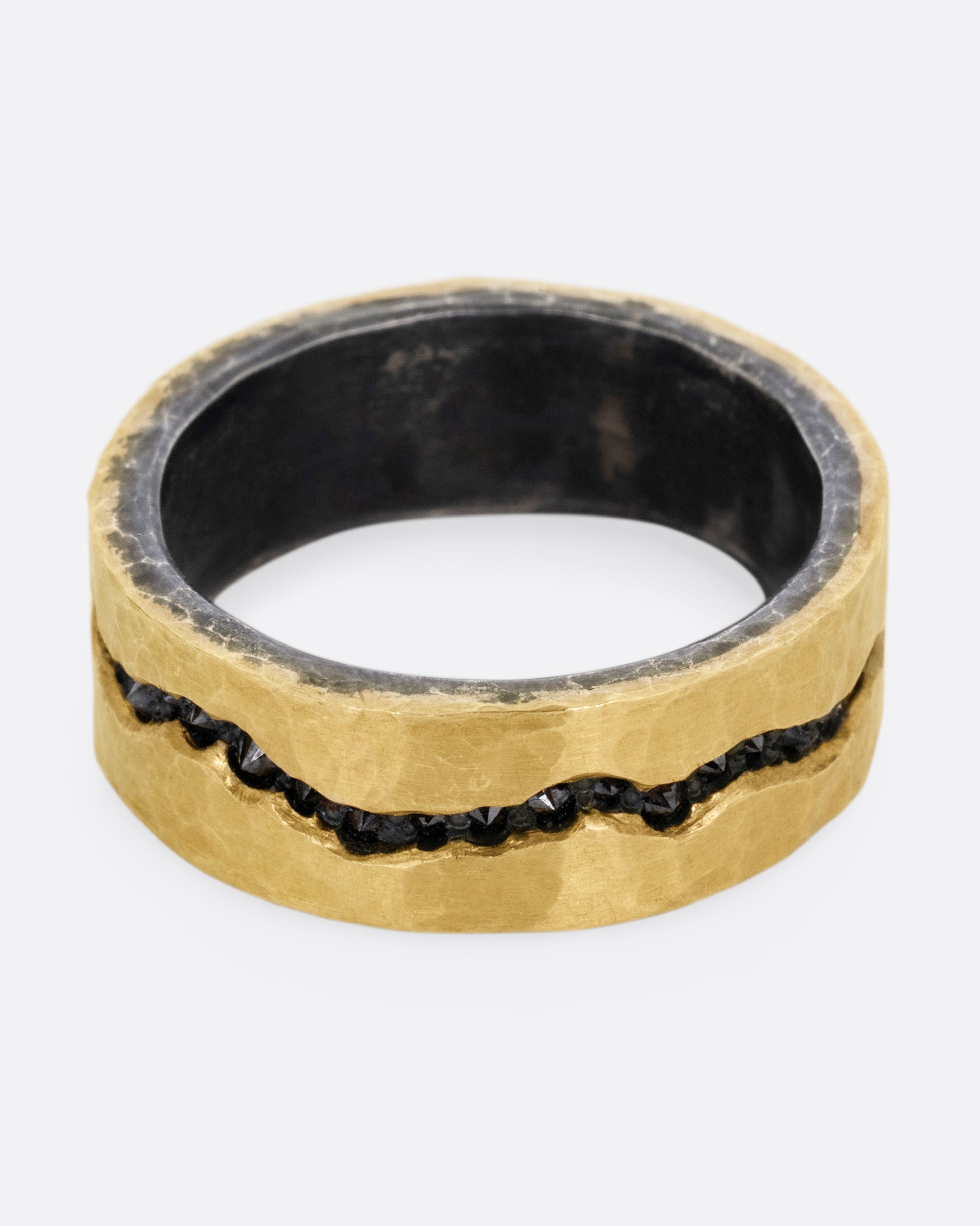 An oxidized silver ring with hammered yellow gold finish and a darkened fissure filled with inverted black diamonds, shown from the front.