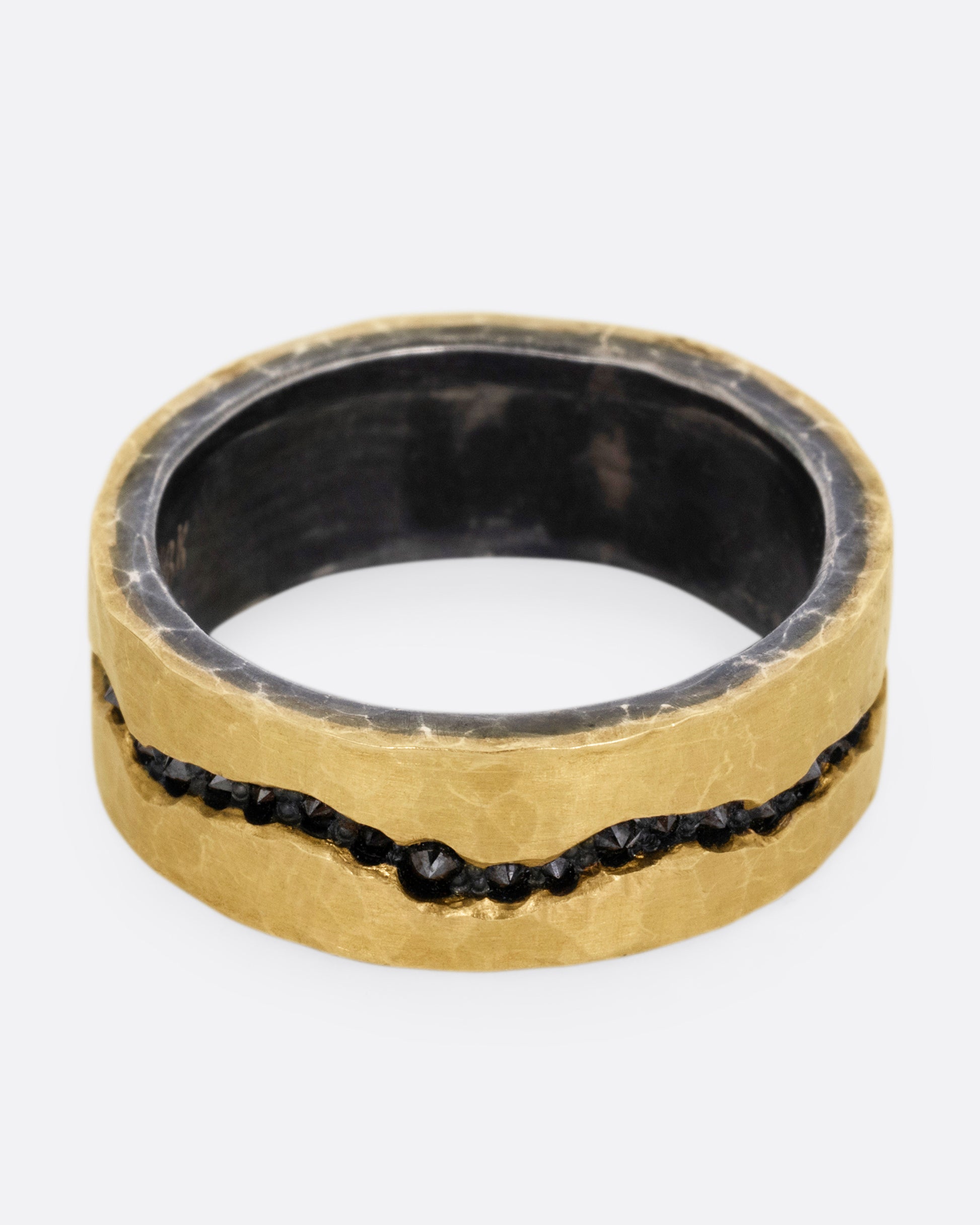 An oxidized silver ring with hammered yellow gold finish and a darkened fissure filled with inverted black diamonds, shown from the front.