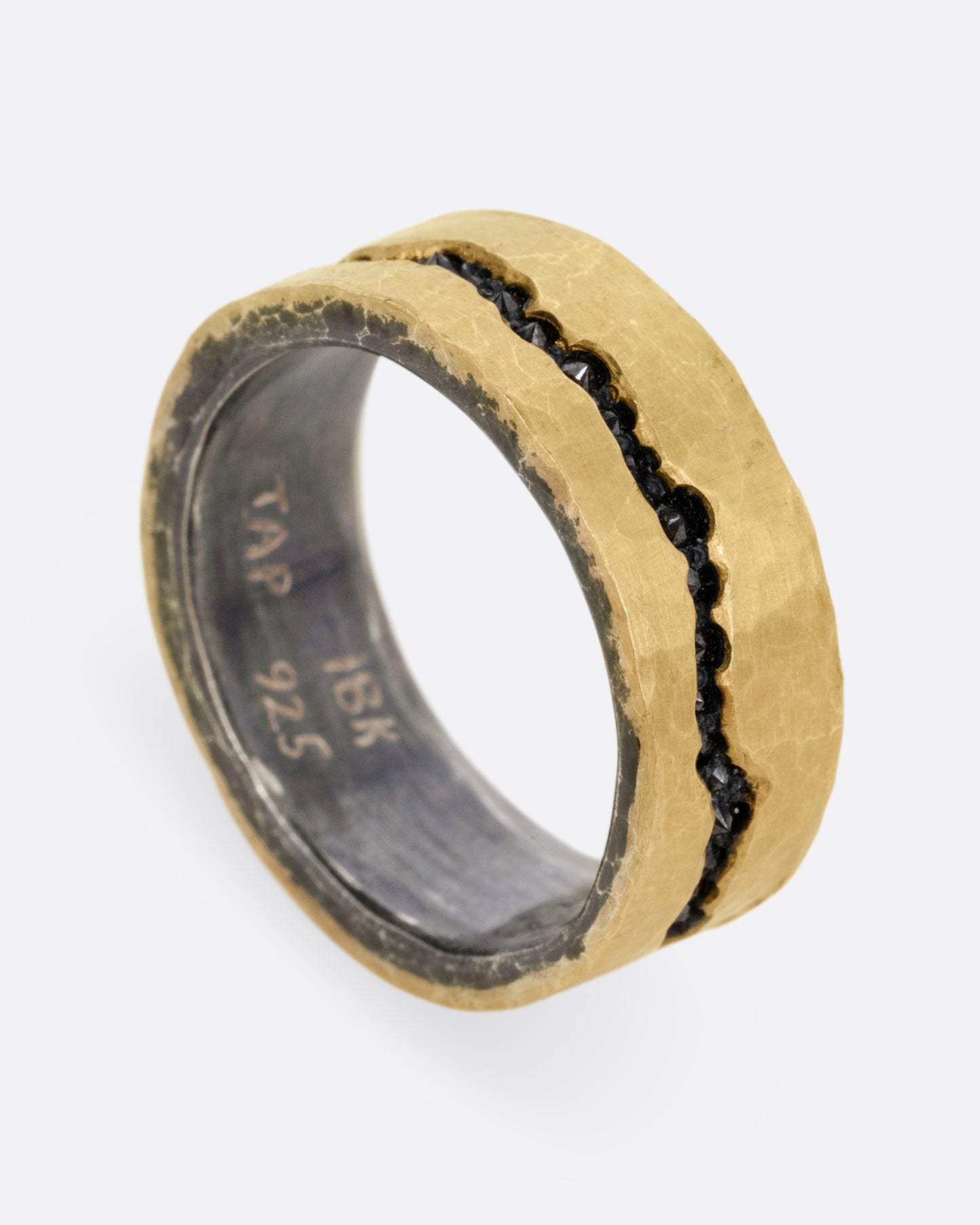 An oxidized silver ring with hammered yellow gold finish and a darkened fissure filled with inverted black diamonds, shown standing up from the side.