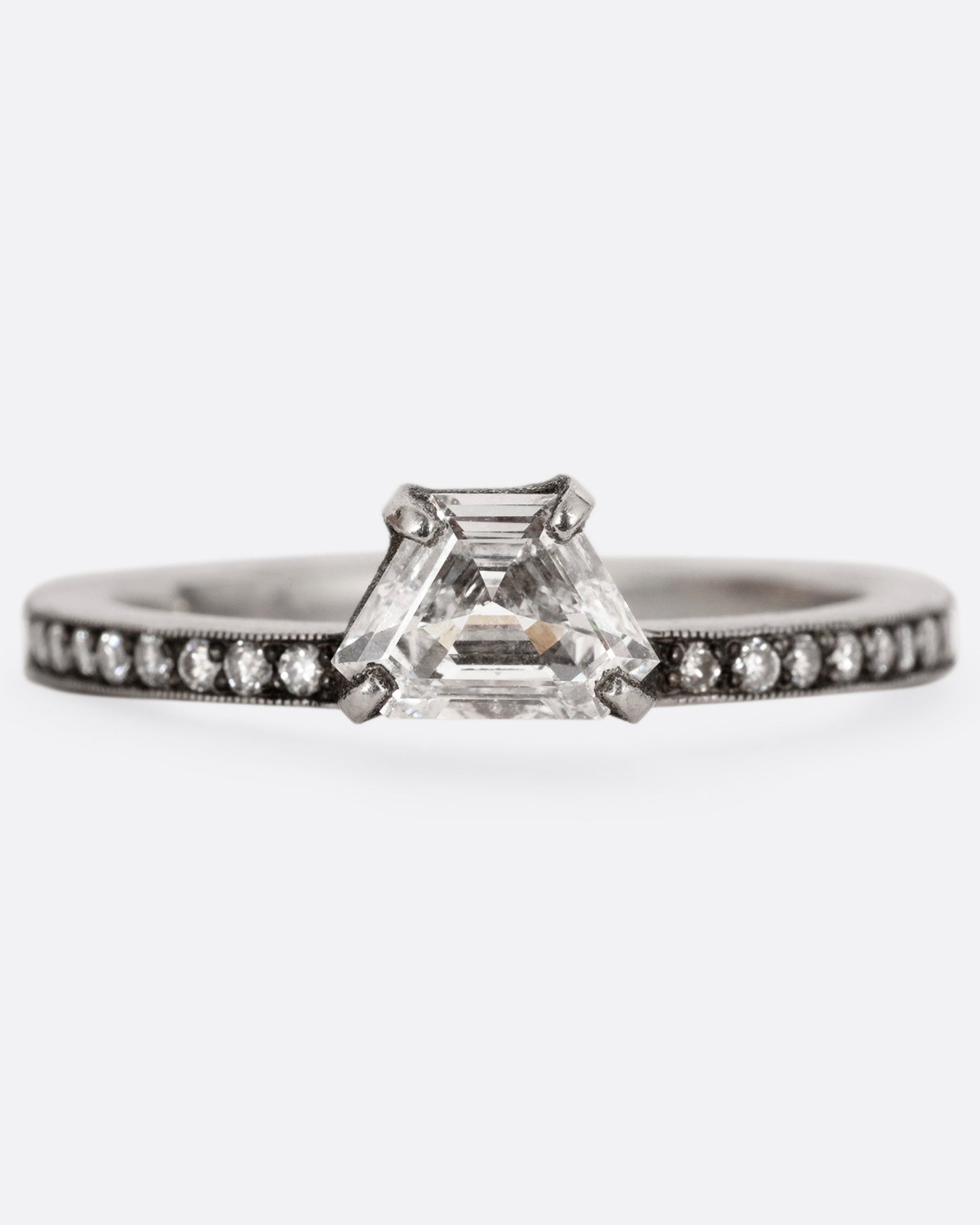 A platinum band with pave diamonds all the way around and a solitaire trapeze diamond. Shown from the front.