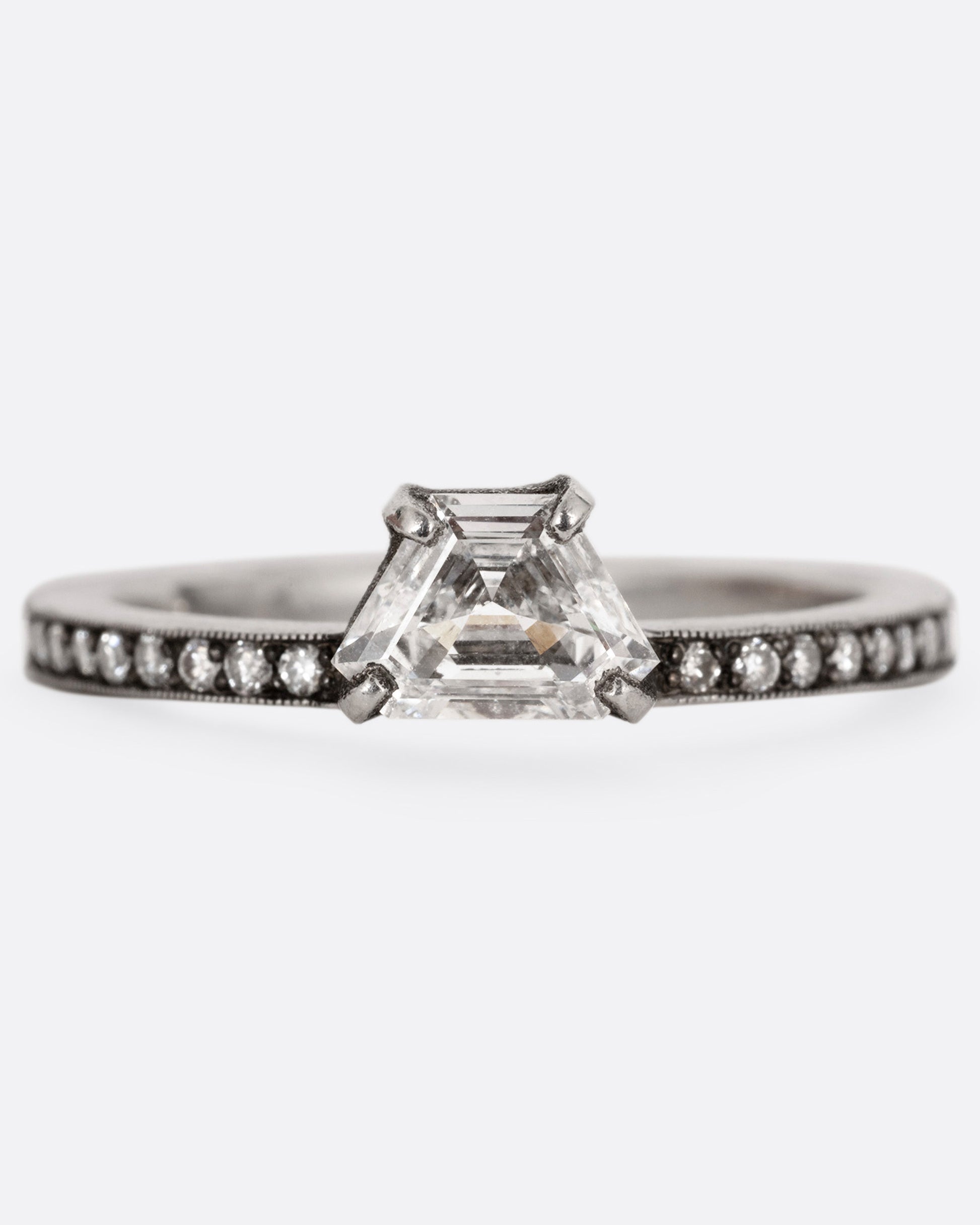 A platinum band with pave diamonds all the way around and a solitaire trapeze diamond. Shown from the front.