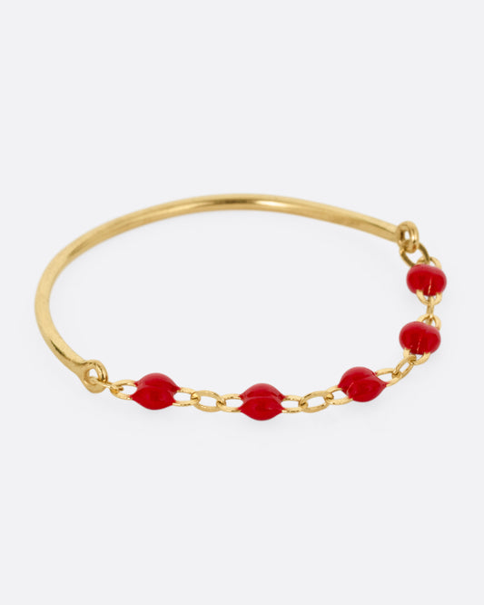 A yellow gold ring with a solid back and cable chain front with red resin droplets. Shown from the side.