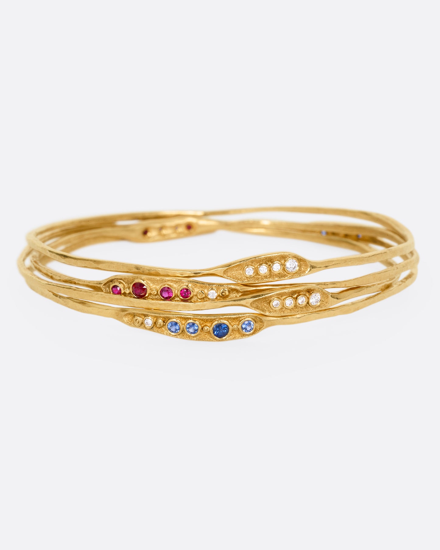 A stack of yellow gold bracelets with rubies, sapphires, and diamonds, shown from the front.