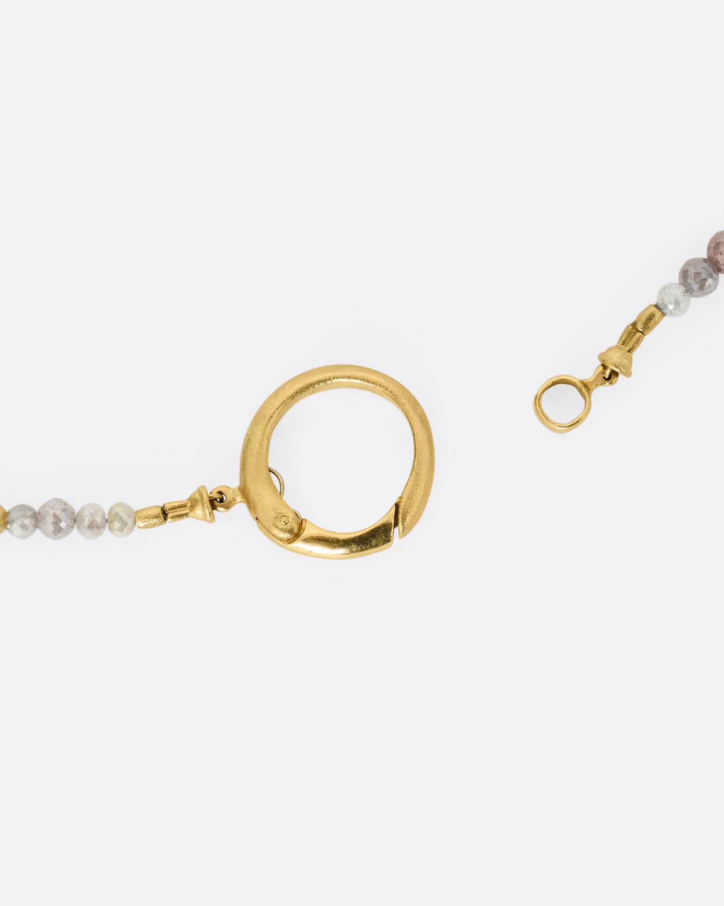 A close up of a multicolored diamond beaded necklace with a yellow gold charm holder.