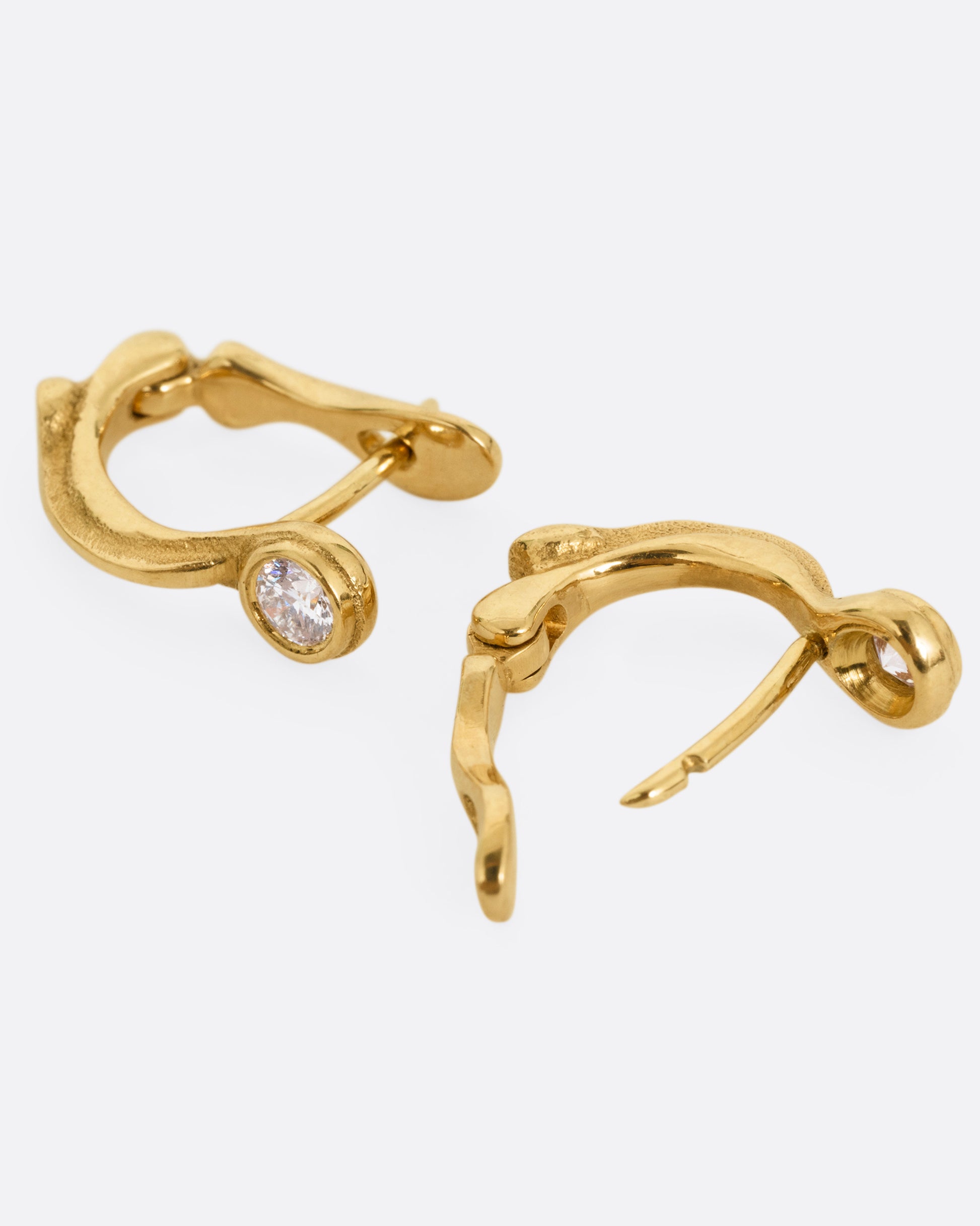 A pair of yellow gold hoop earring with brilliant cut diamonds, shown lying on their sides with one hoop open.