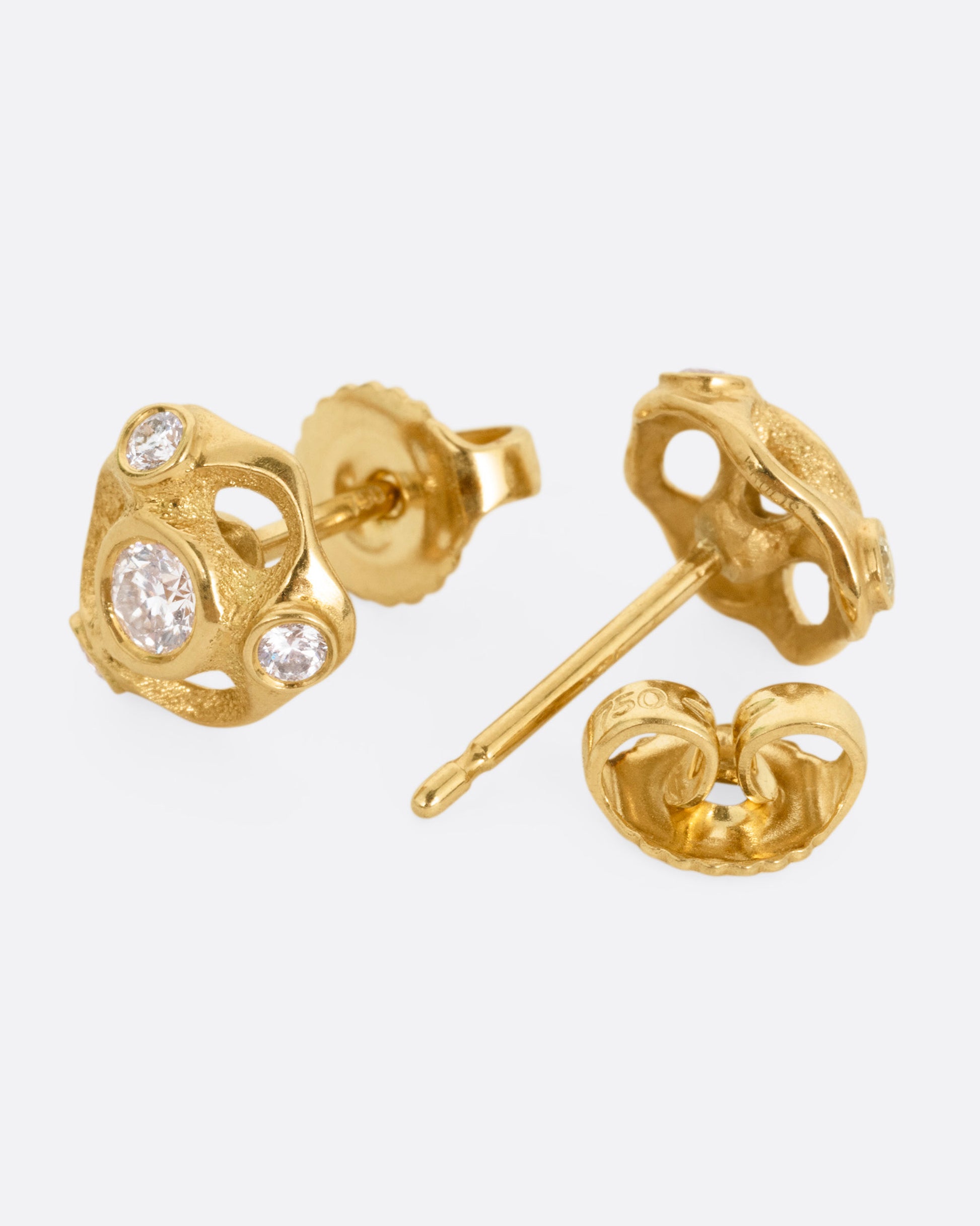 A pair of yellow gold stud earrings with four brilliant cut diamonds in each. One is shown from the front, the other is shown open from the back.