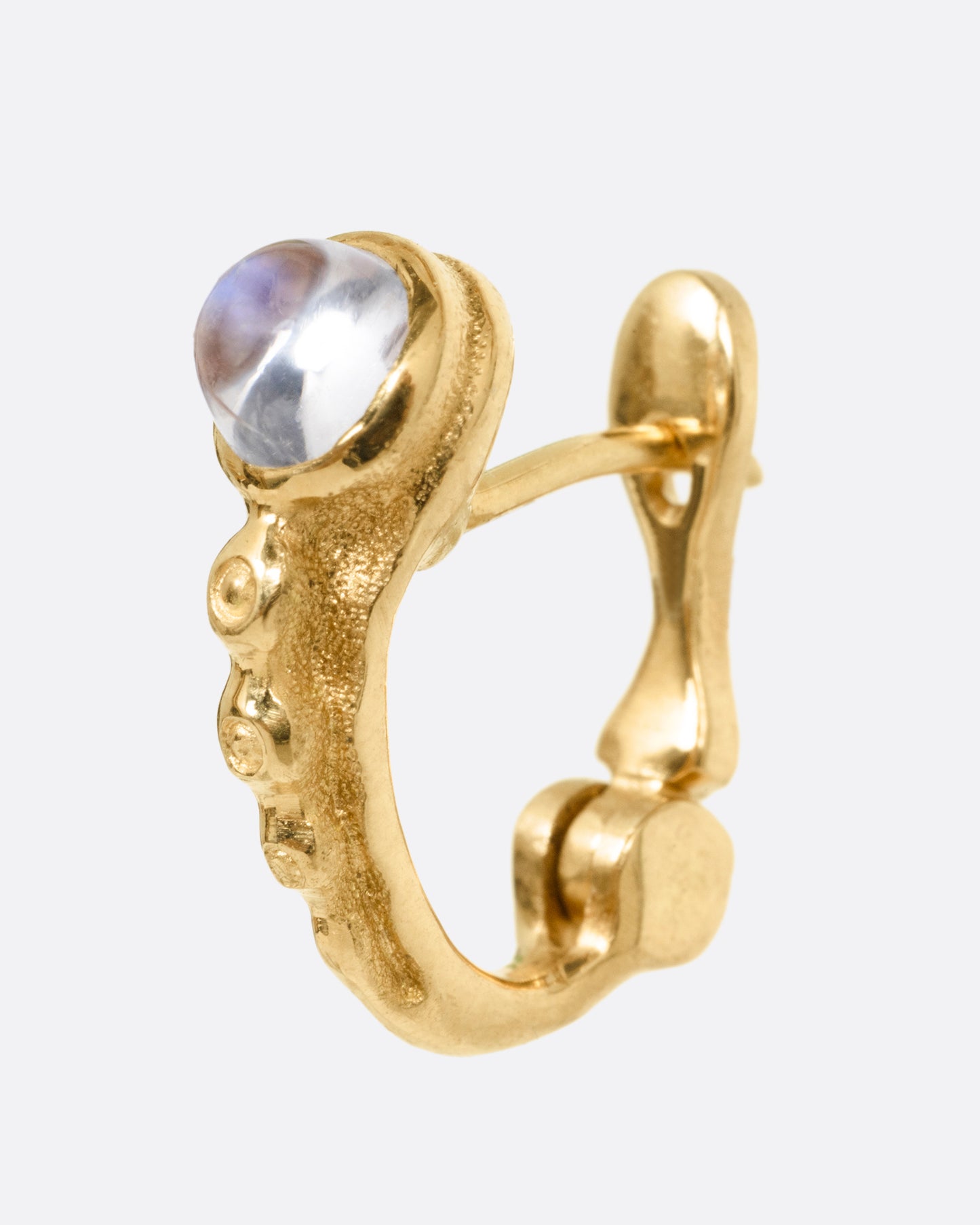 A yellow gold hoop earring with granulation and a moonstone. Shown from the side.