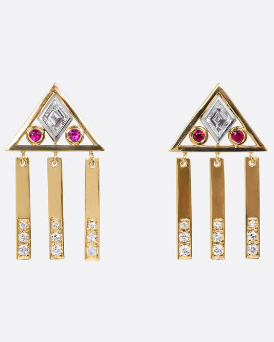 A yellow gold pair of stud back earrings with triangular tops set with lozenge cut diamonds flanked by rubies, and three free moving diamond studded bars on each base. Shown from the front.