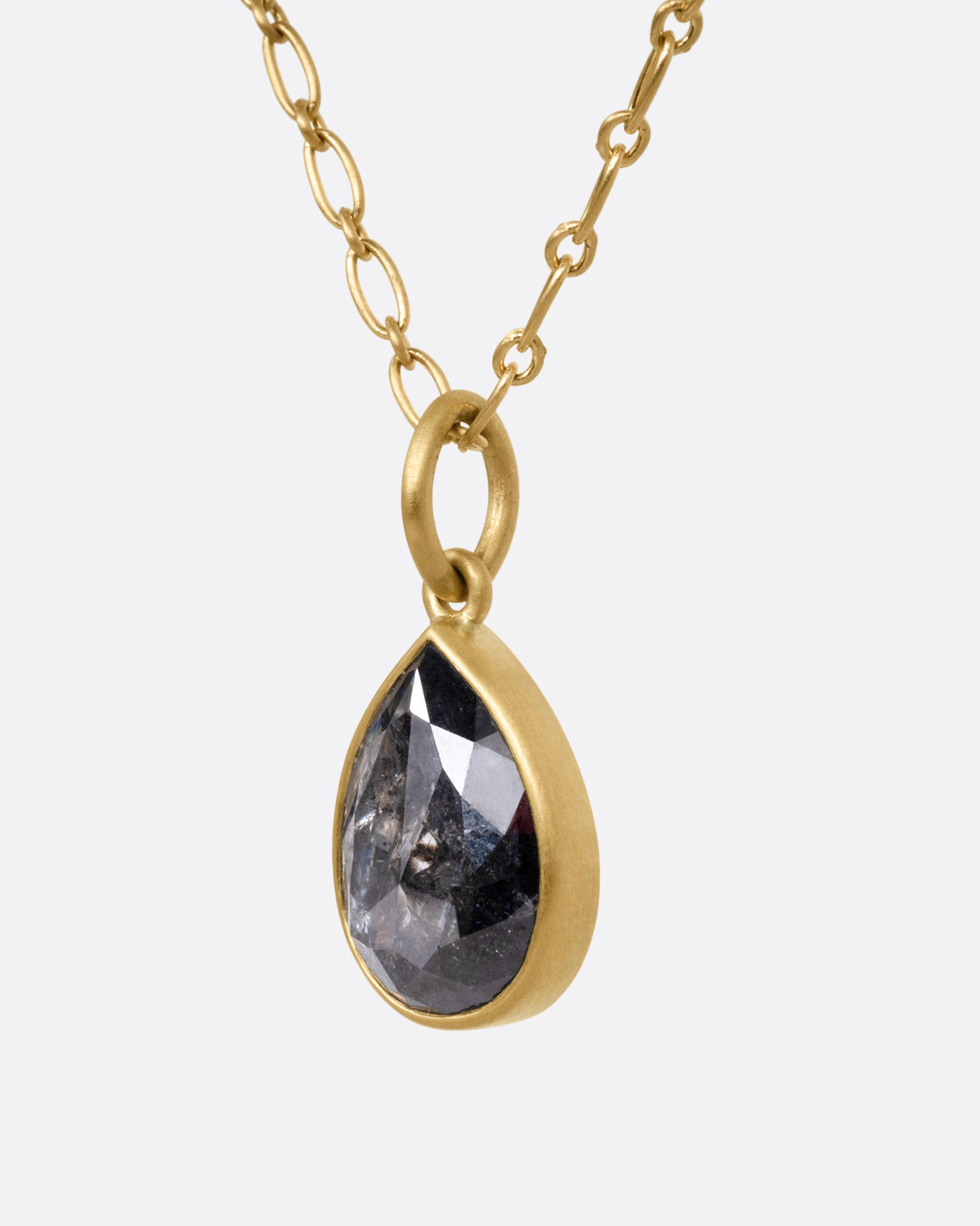 A yellow gold elongated link cable chain necklace with a teardrop shaped salt and pepper diamond, shown from the side.