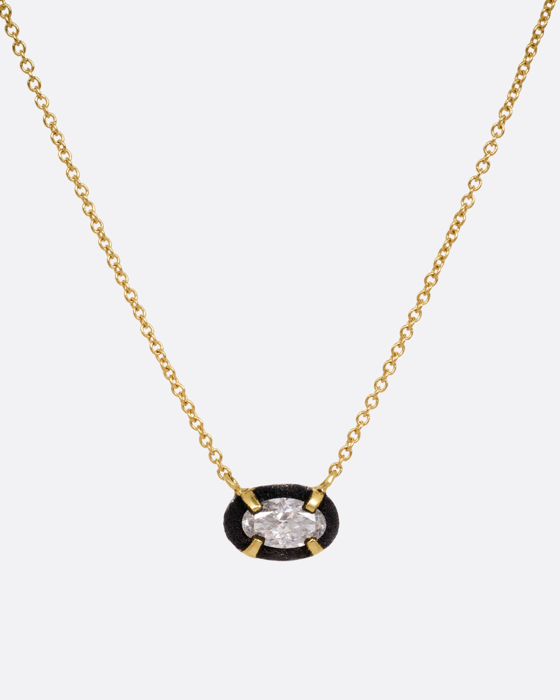 A yellow gold necklace with a pendant of darkened white gold surrounding a prong set diamond, shown from the front.