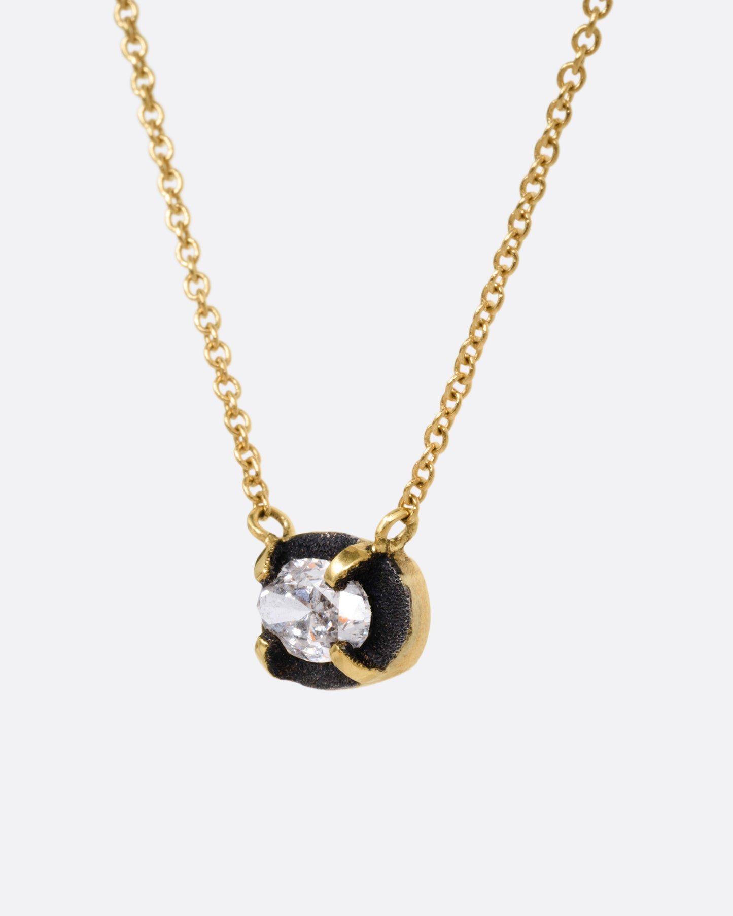 A yellow gold necklace with a pendant of darkened white gold surrounding a prong set diamond, shown from the side.