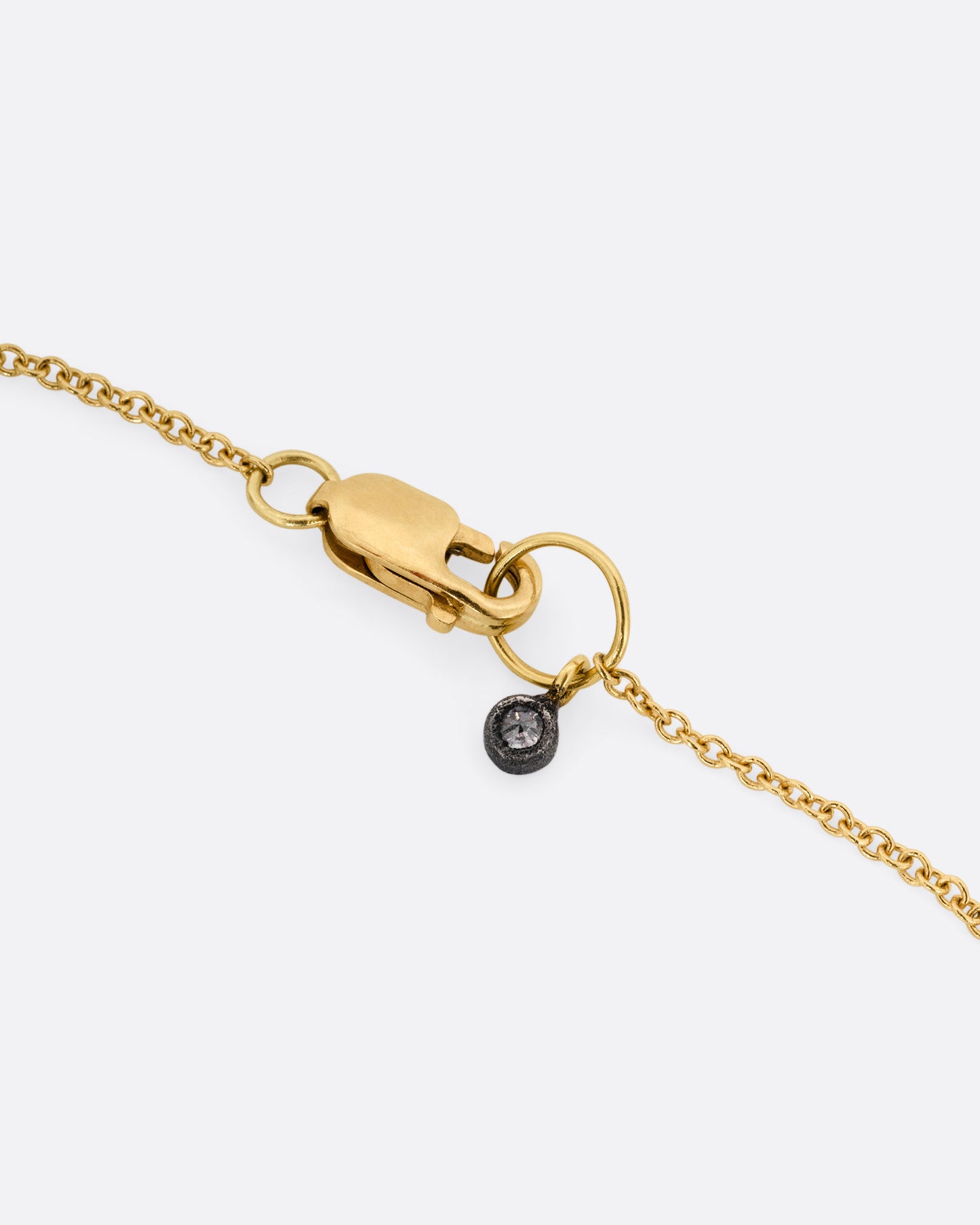 A close up of the clasp of a yellow gold necklace with a tag of darkened white gold and a diamond.